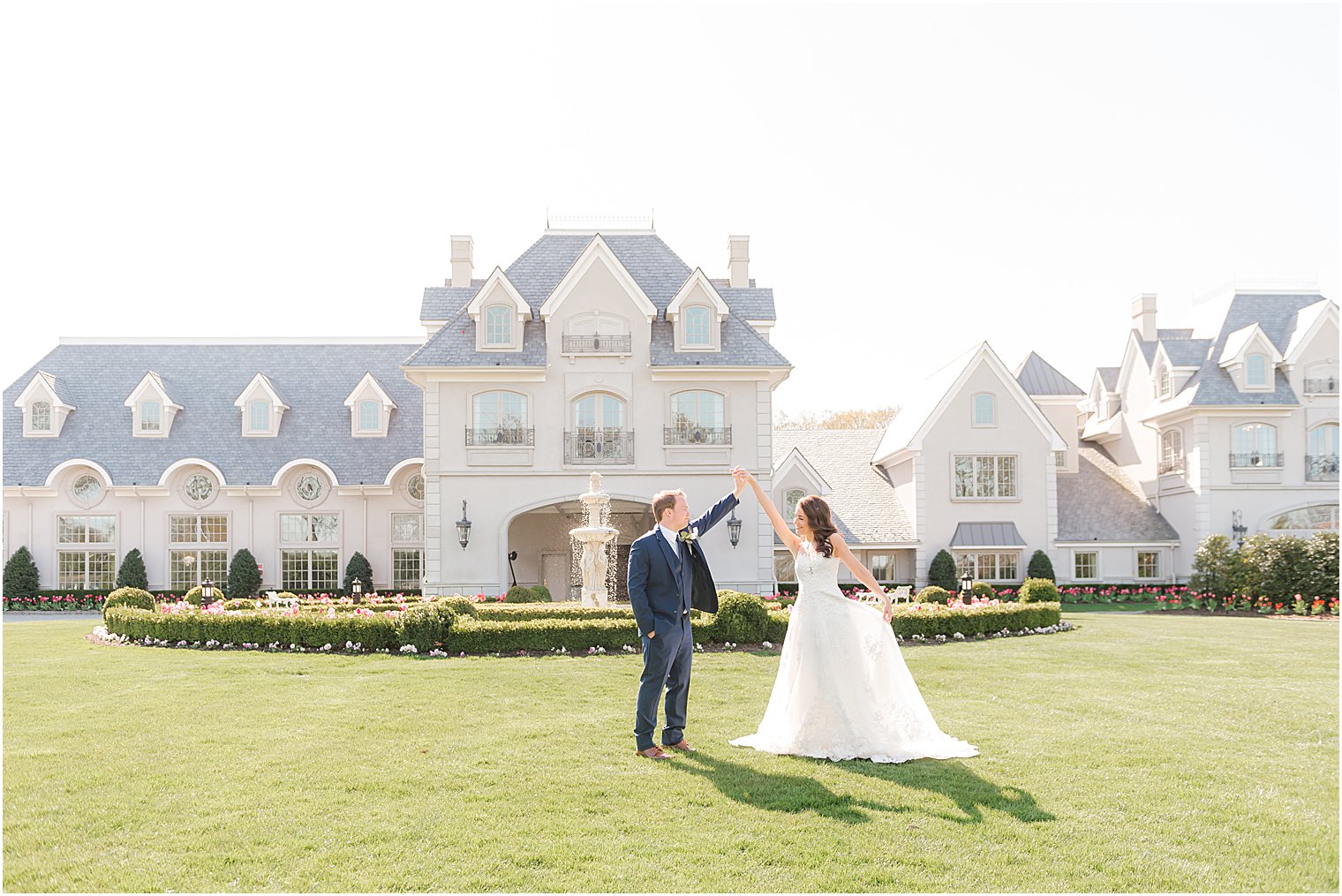 groom twirls bride on lawn outside Park Chateau Estate and Gardens
