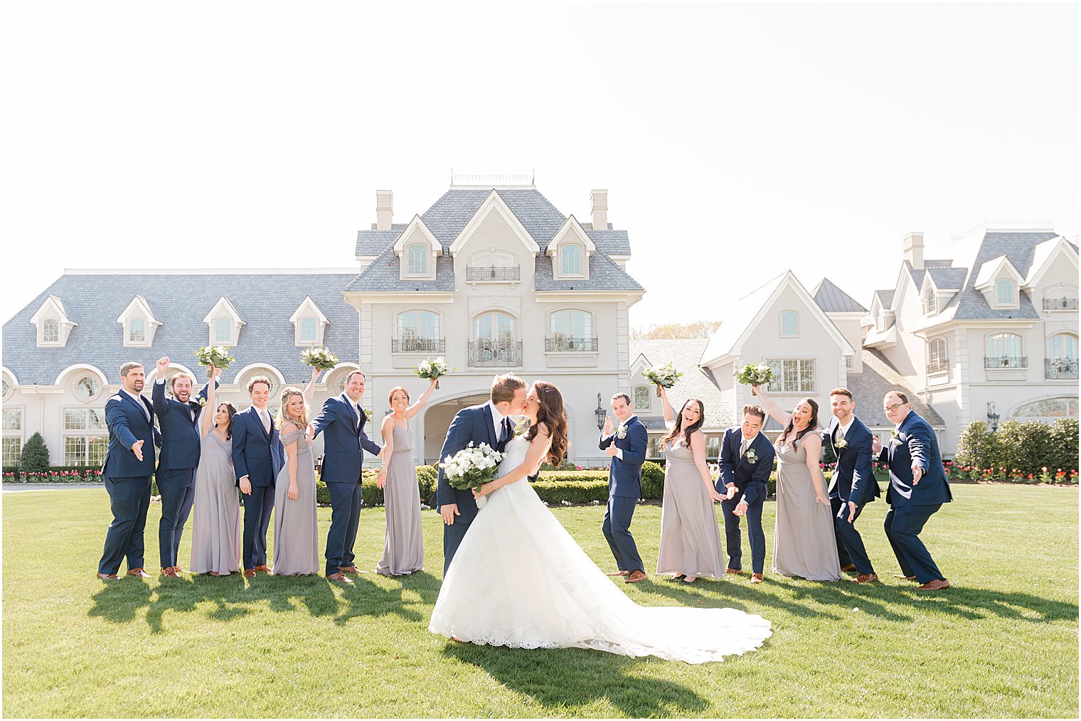 groom kisses bride on the lawn at Park Chateau Estate and Gardens with wedding party around them 