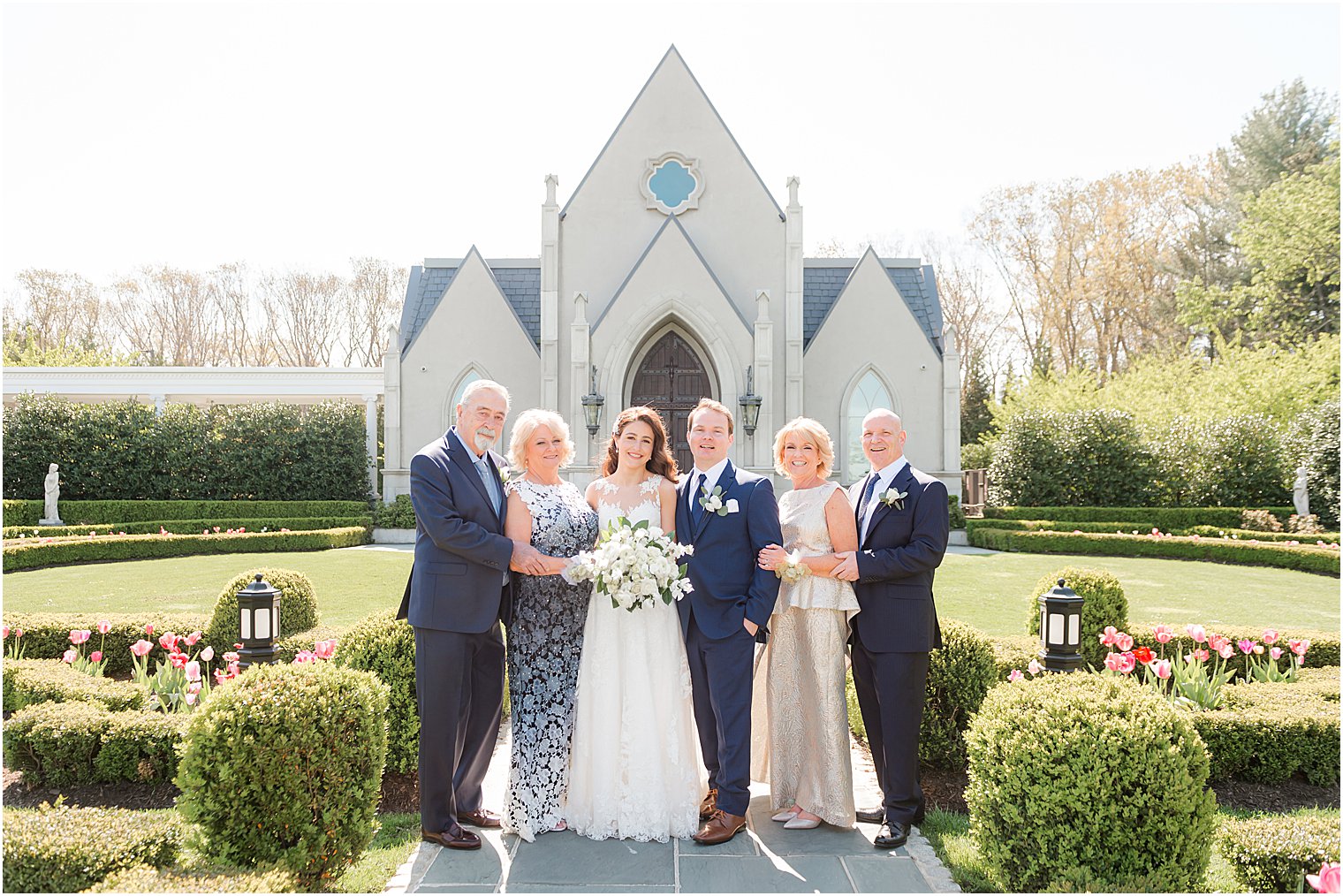 bride and groom pose with parents in front of chapel at Park Chateau Estate