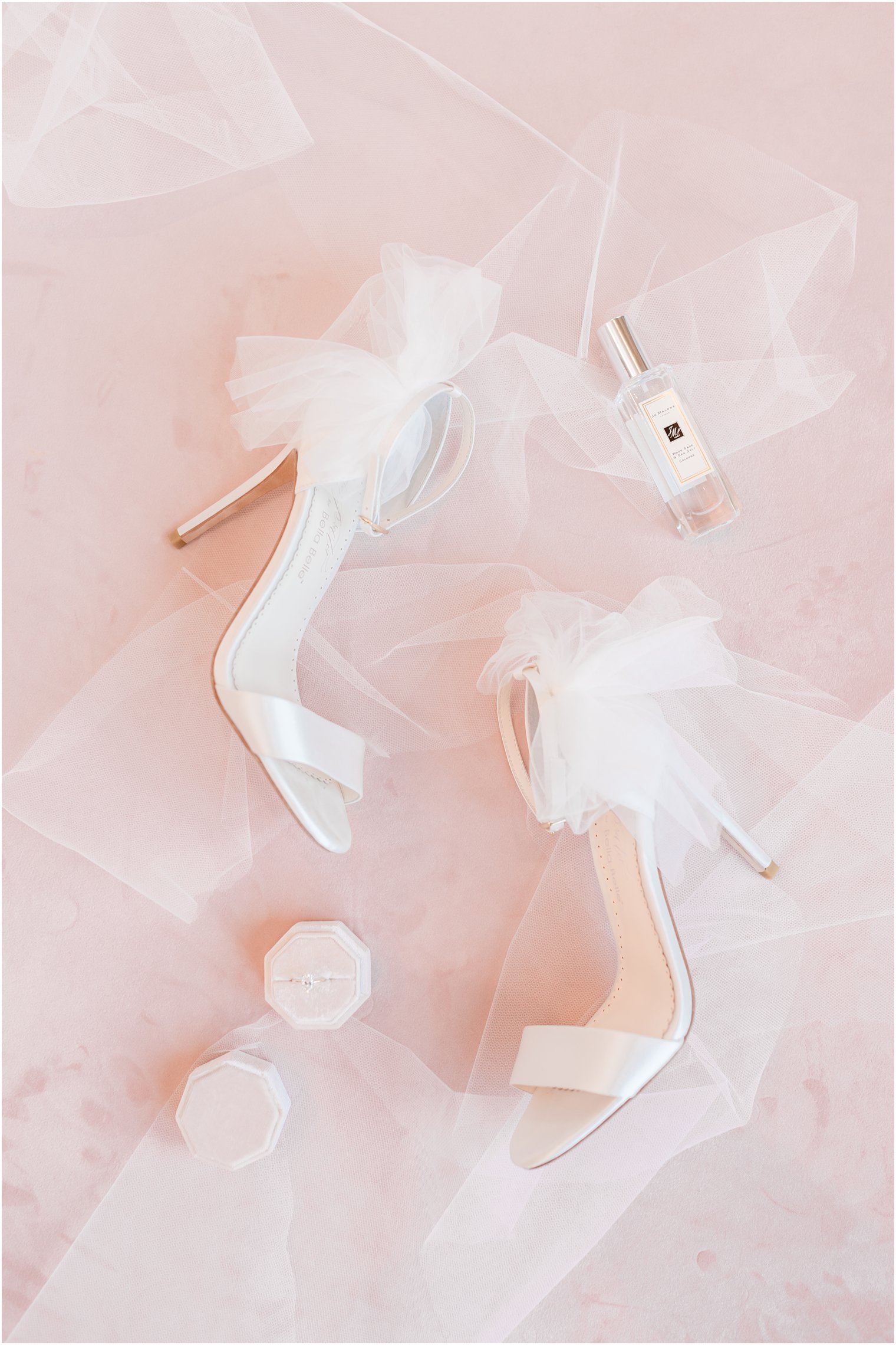 bride's white shoes and rings on pink backdrop