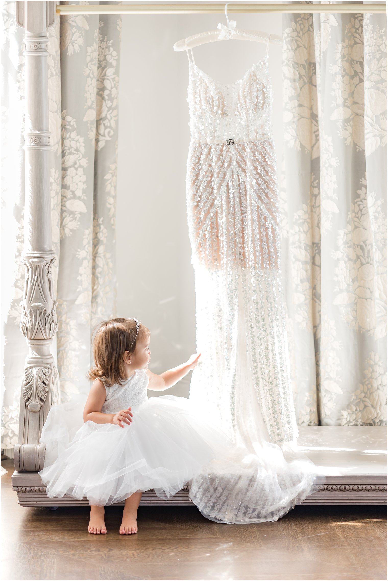 flower girl in white dress sits by bride's reception dress feeling the beading 