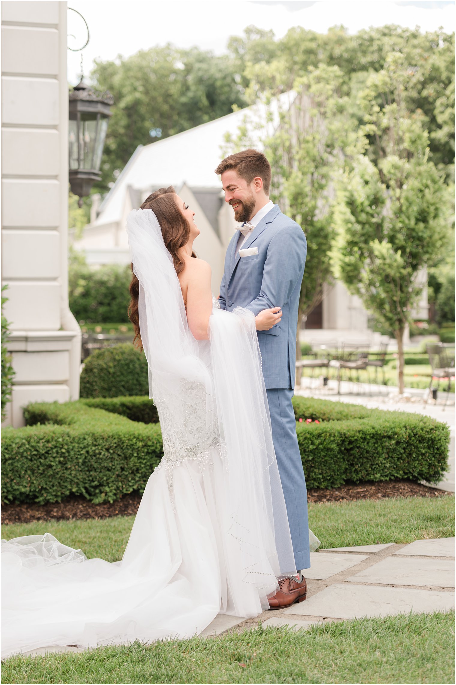 bride holds veil on arm laughing with groom during first look near house of Park Chateau 