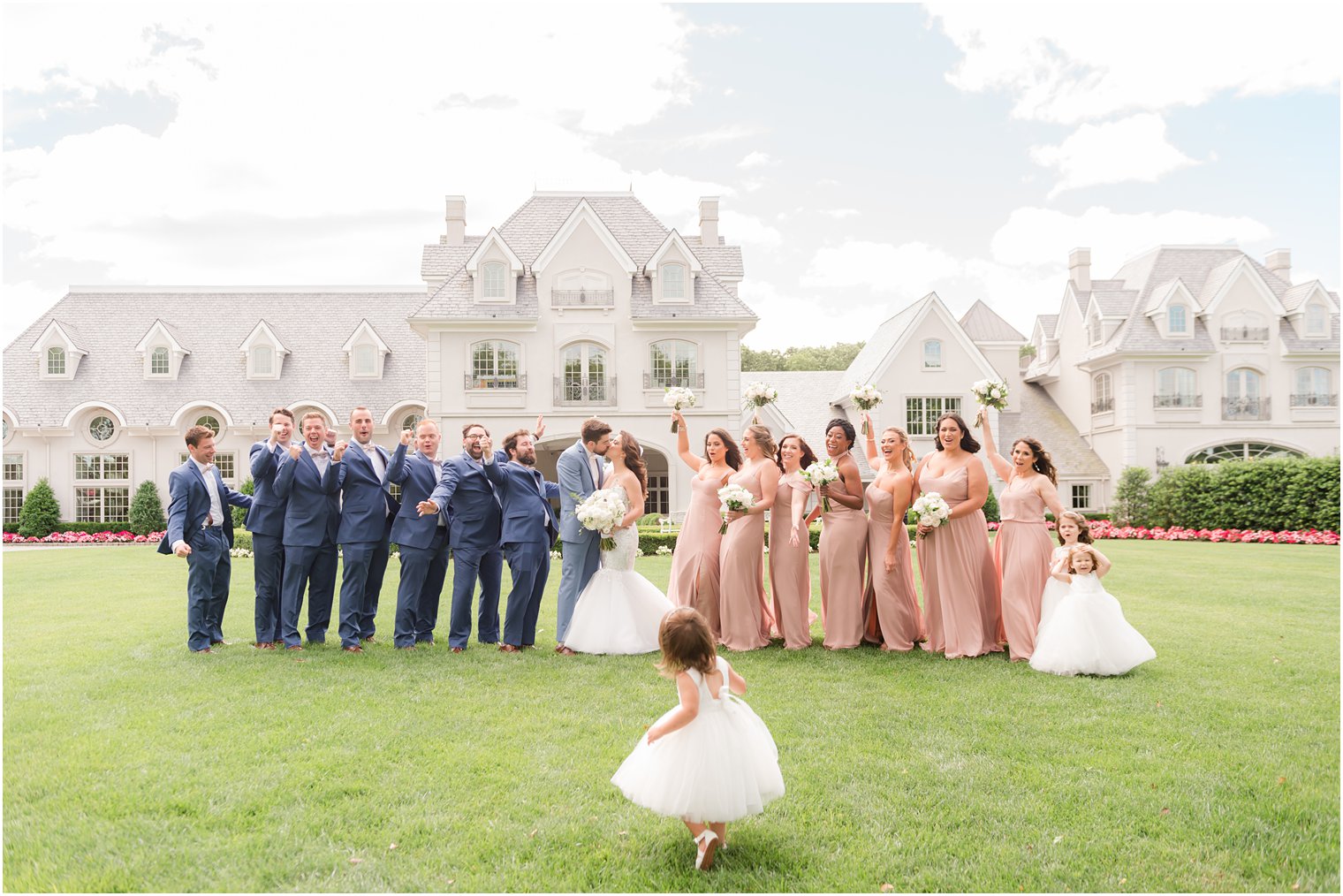 bride and groom kiss on lawn at Park Chateau with bridal party in pink and blue cheering for them 