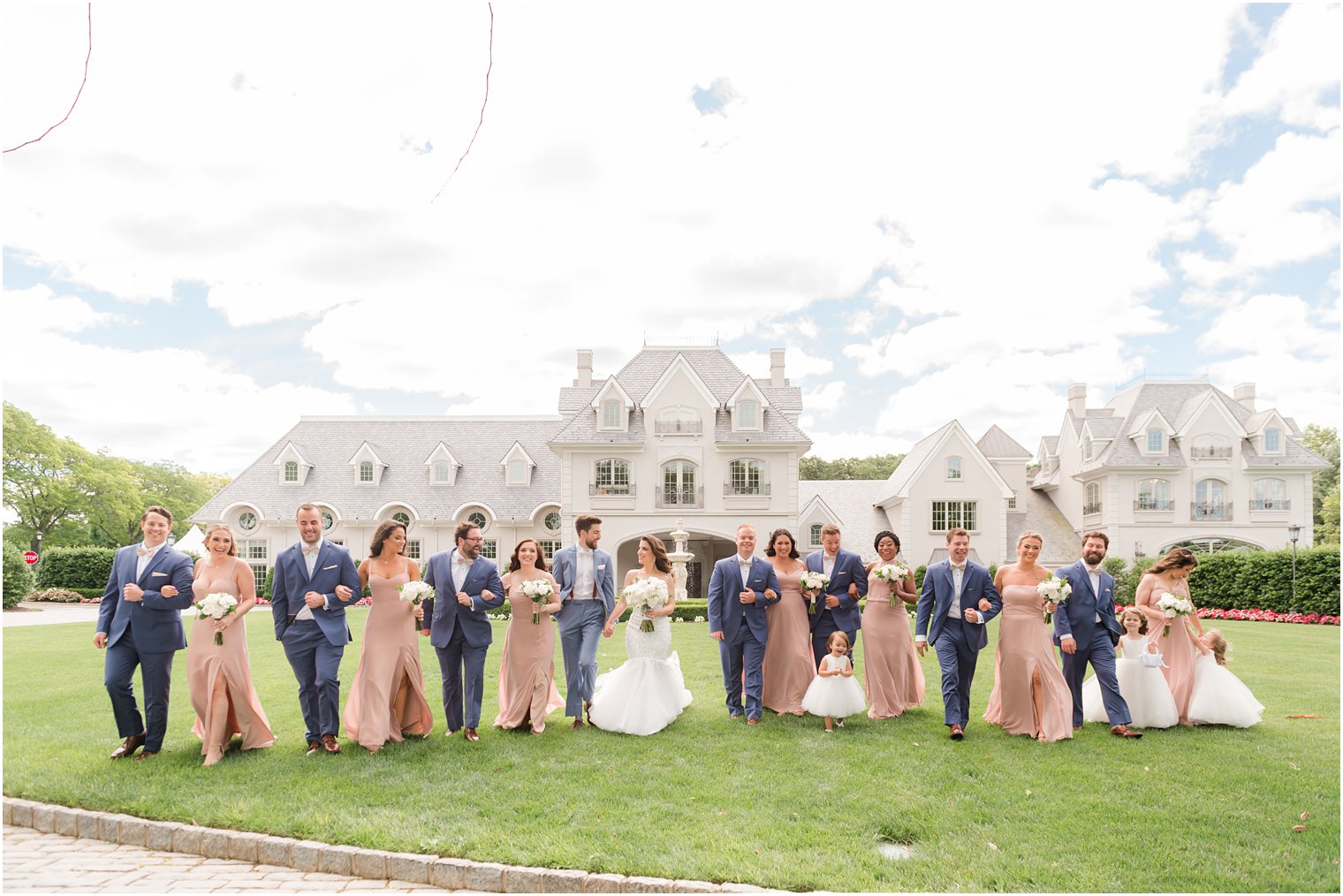 bride and groom walk with wedding party in pink and navy on lawn at Park Chateau 