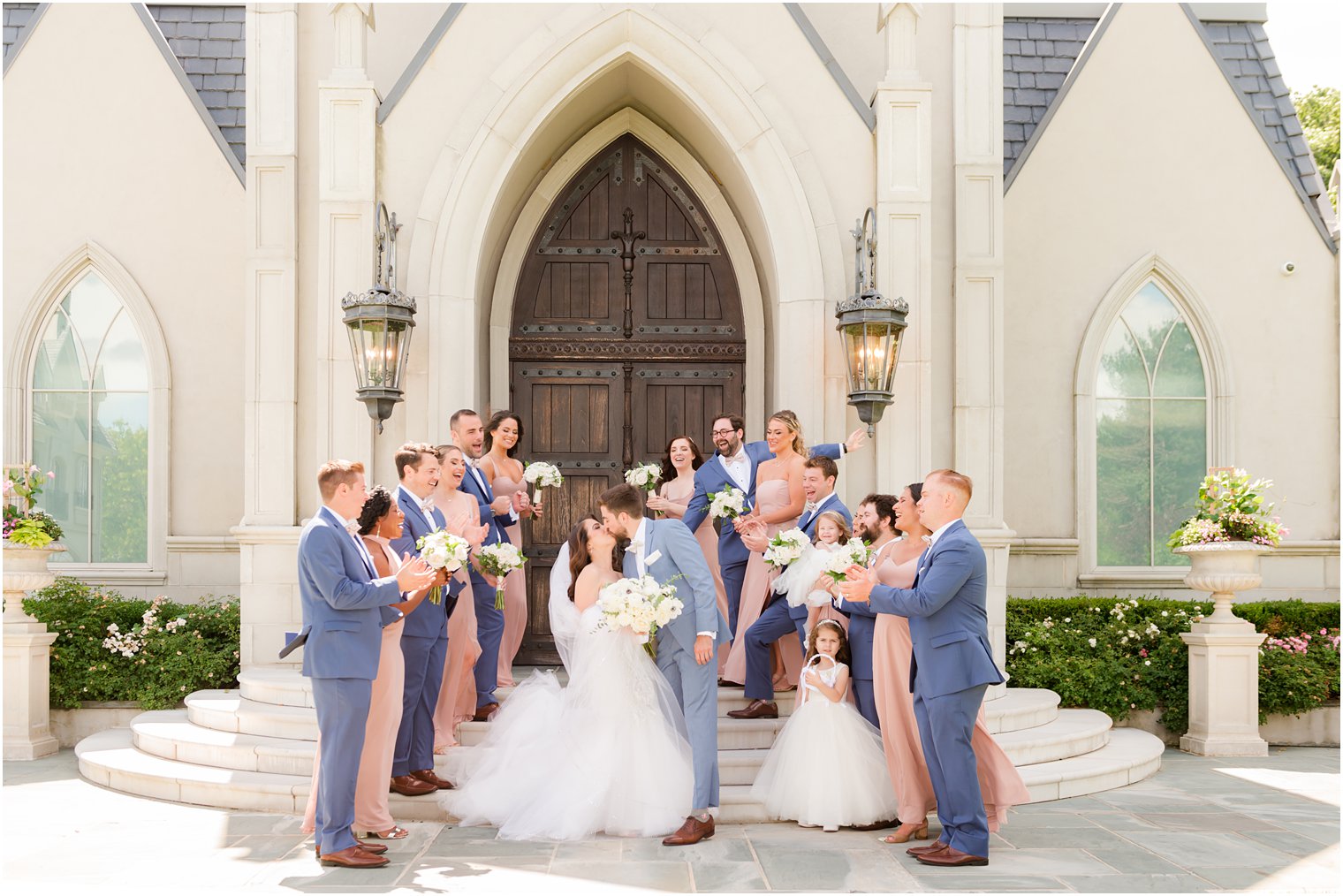 bride and groom kiss in front of wooden doors at Park Chateau chapel with wedding party in navy and pink cheering 