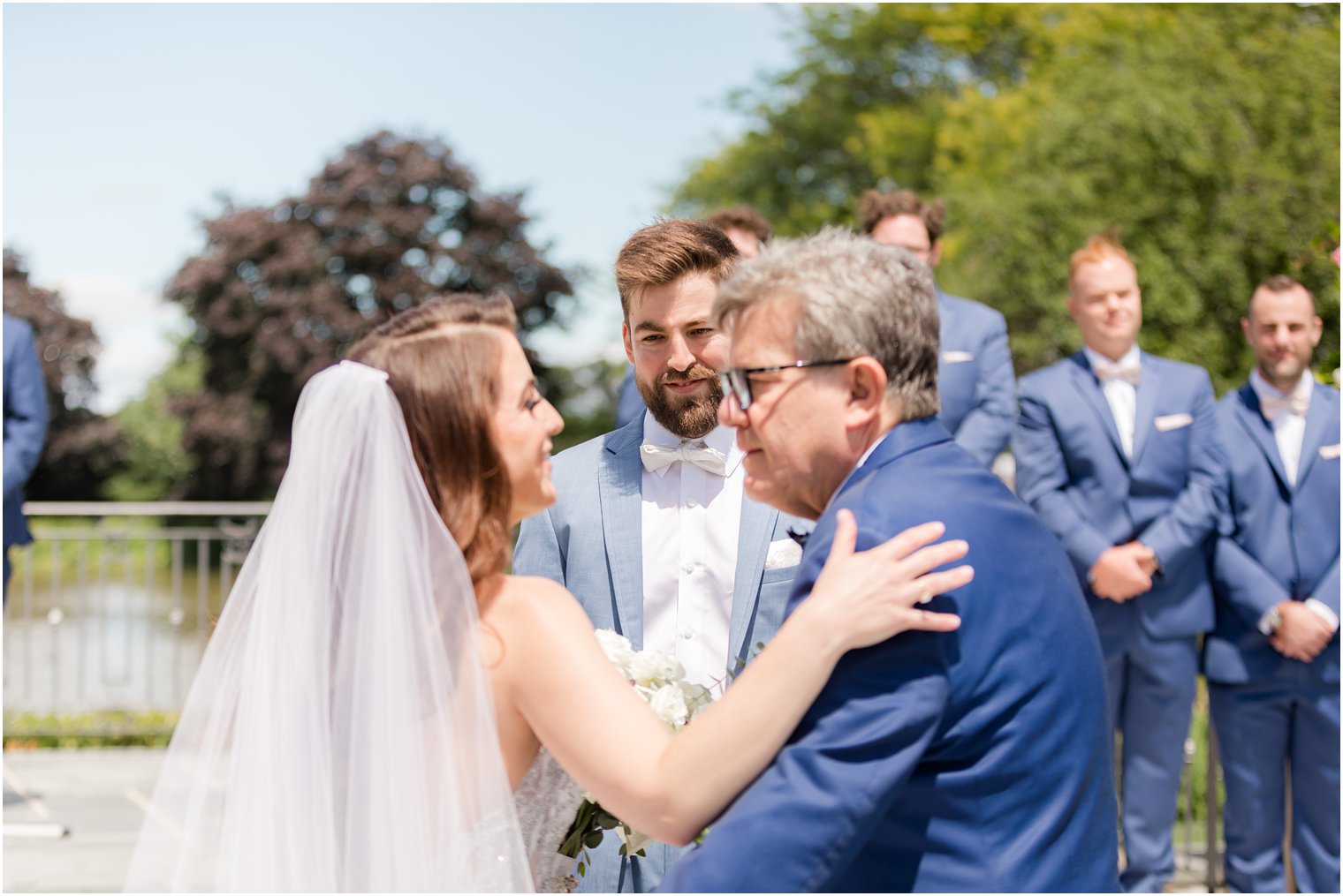 groom smiles at bride and father during wedding ceremony 