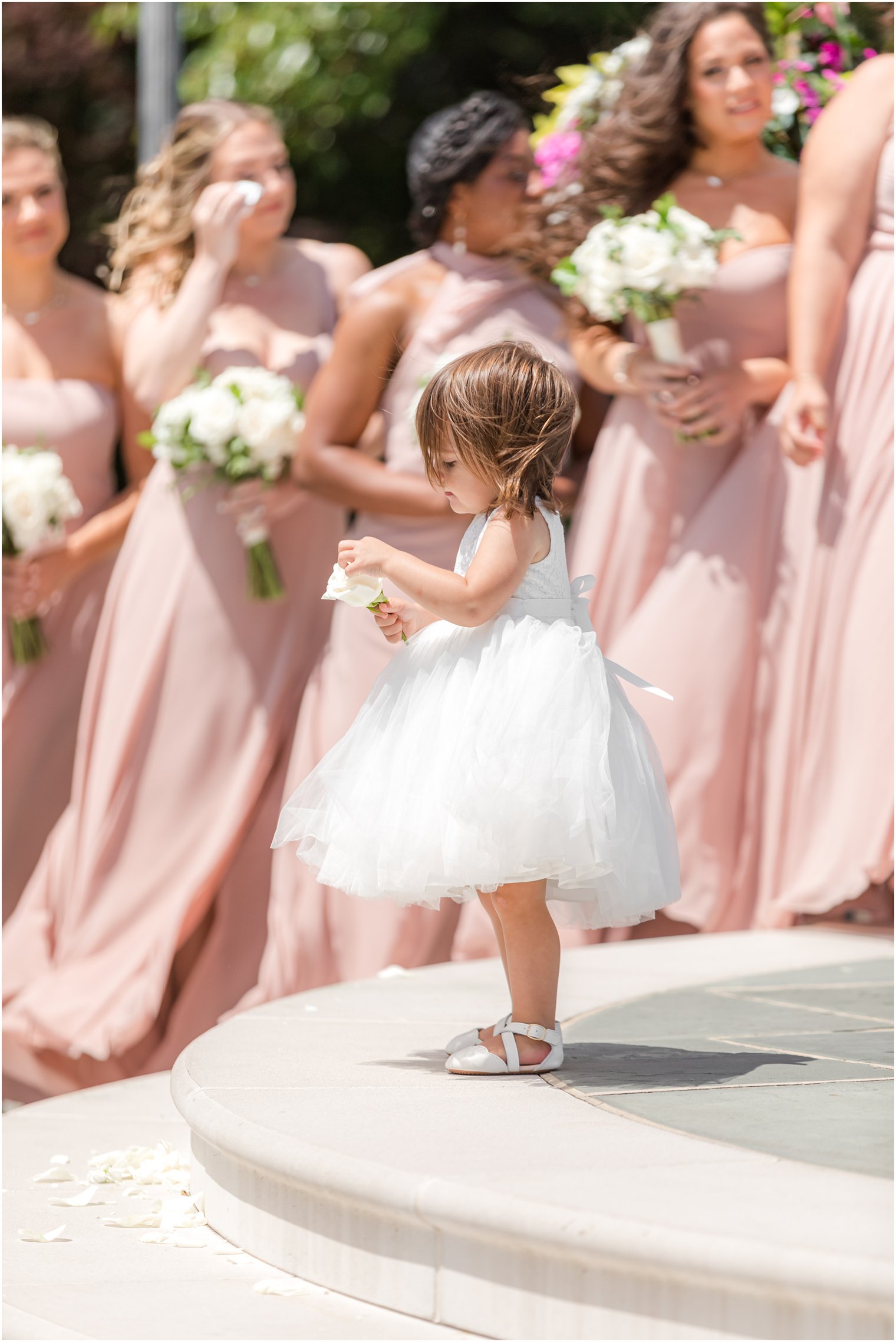 flower girl in white dress plays with white rose
