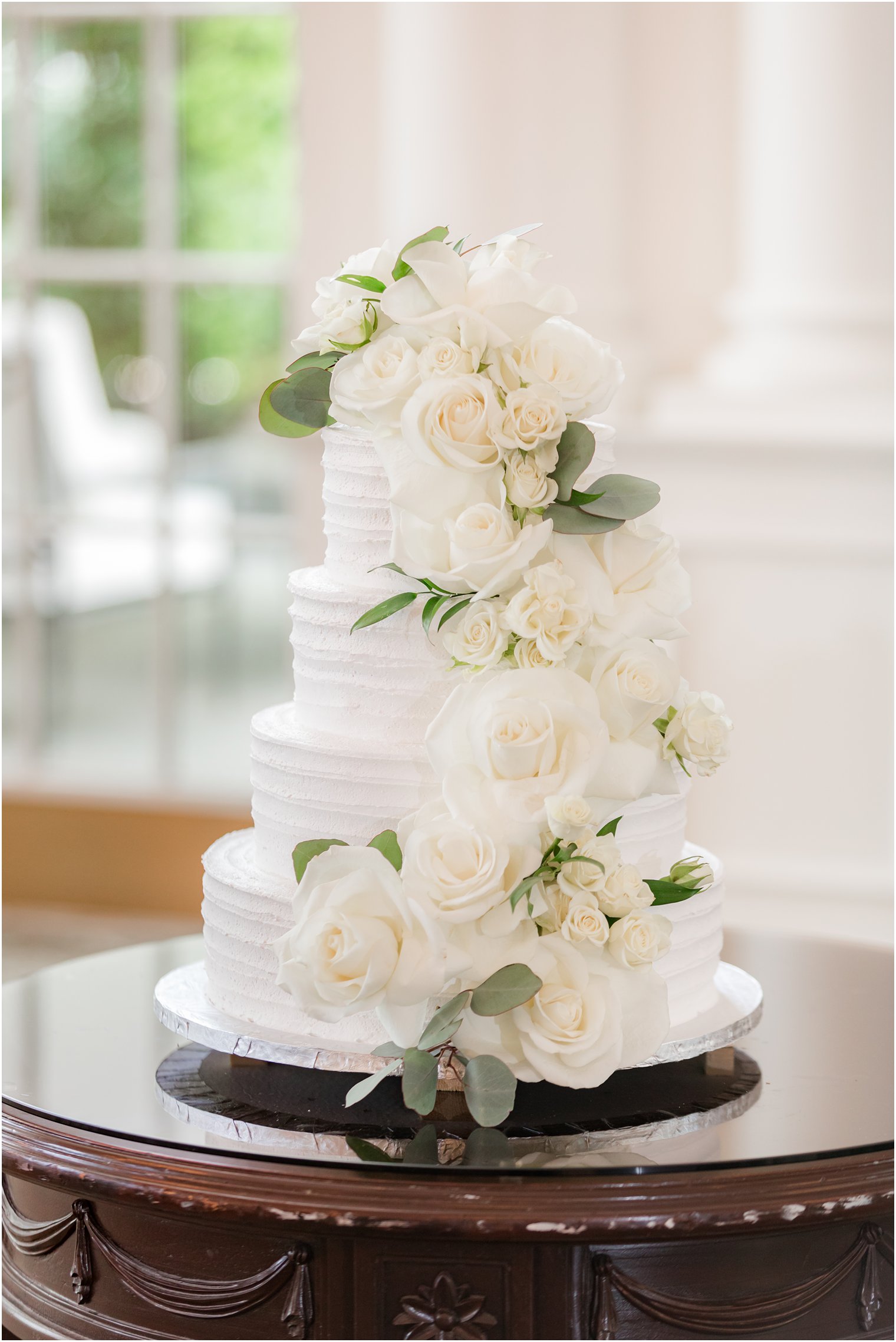 tiered wedding cake with white icing and cascading ivory flowers 