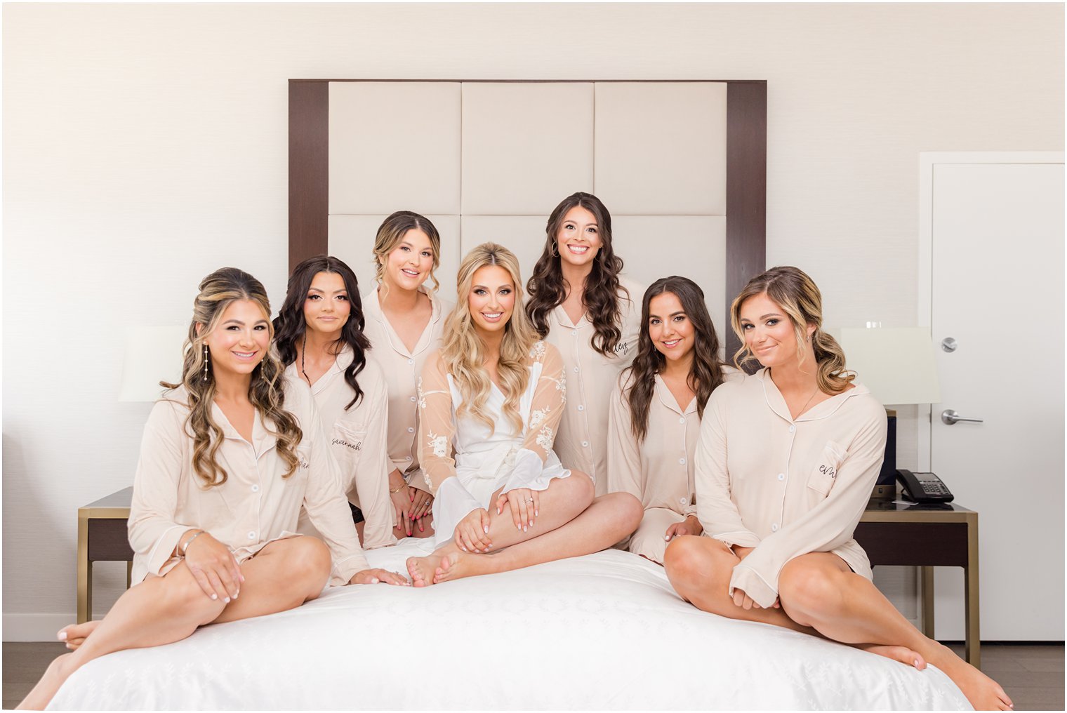 bride sits with bridesmaids in matching long sleeve pajamas on bed at hotel 