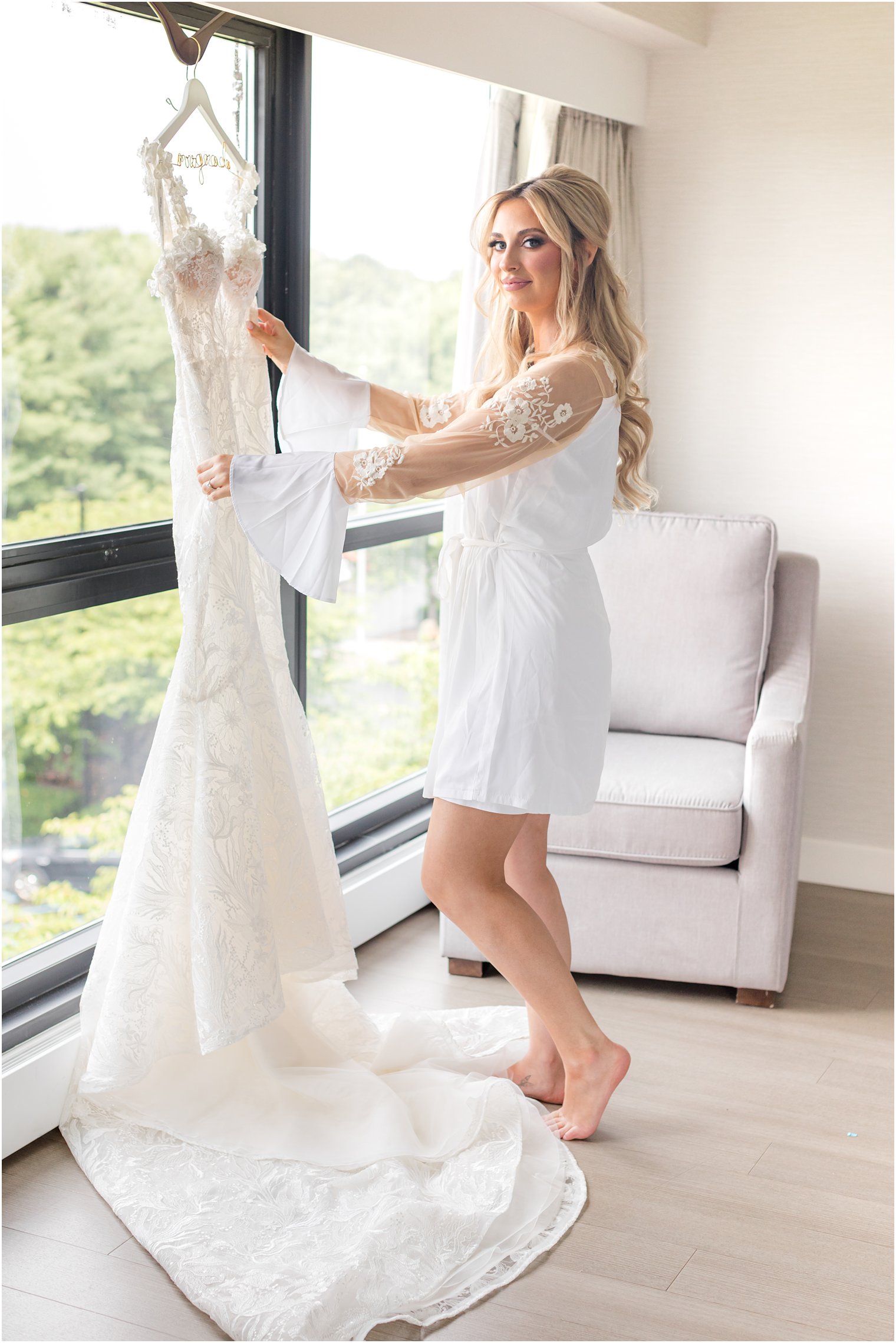 bride in lace robe looks at wedding gown hanging in window of NJ hotel 
