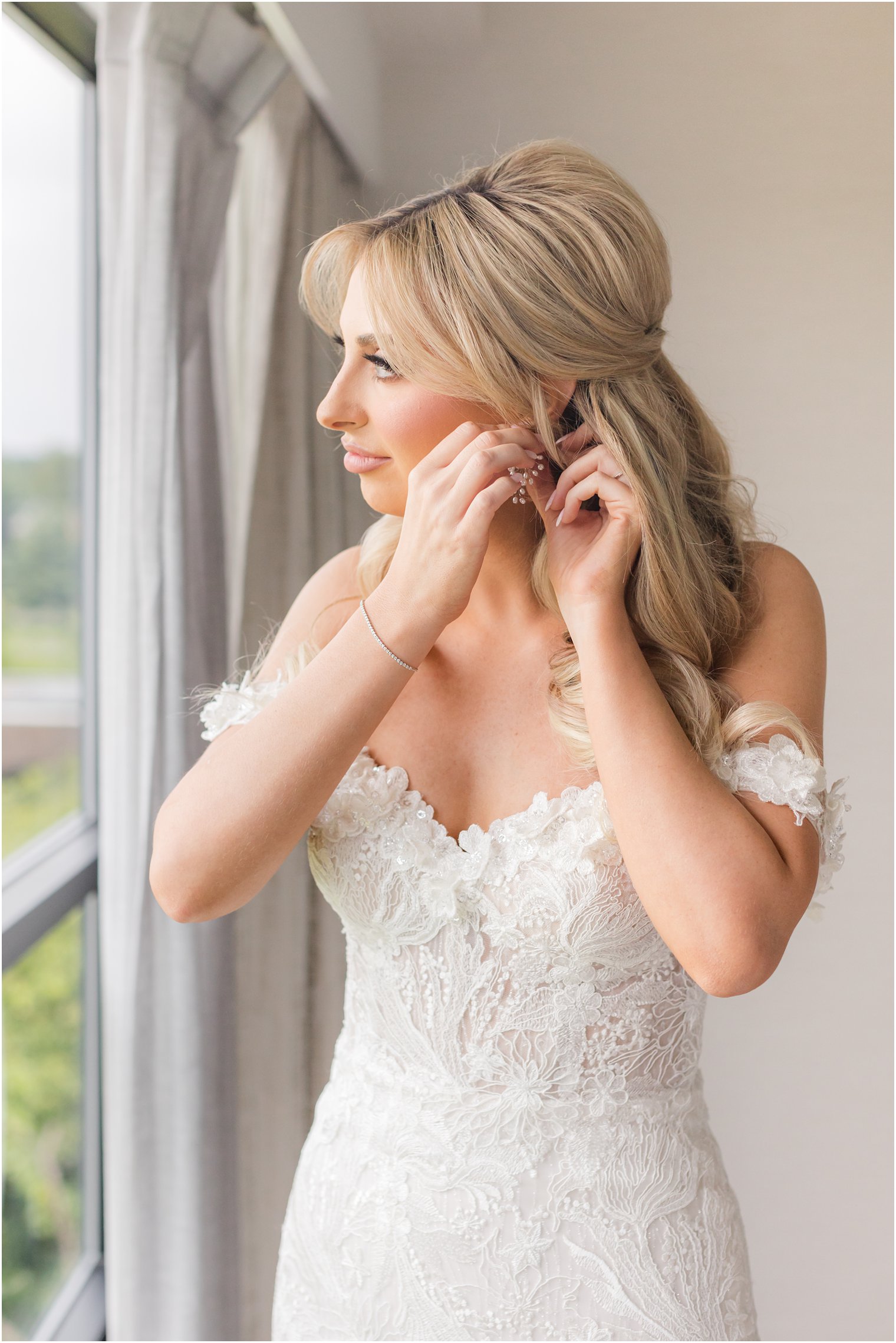 bride in strapless wedding gown with lace sleeves adjusts earrings