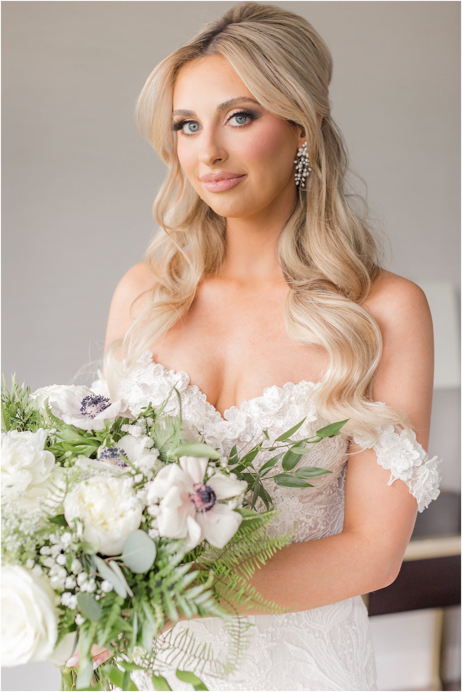 bride sits in strapless wedding gown with lace detailing n bodice holding ivory bouquet 