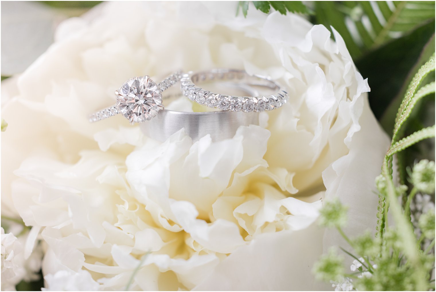 diamond and silver wedding bands rest on ivory peony 