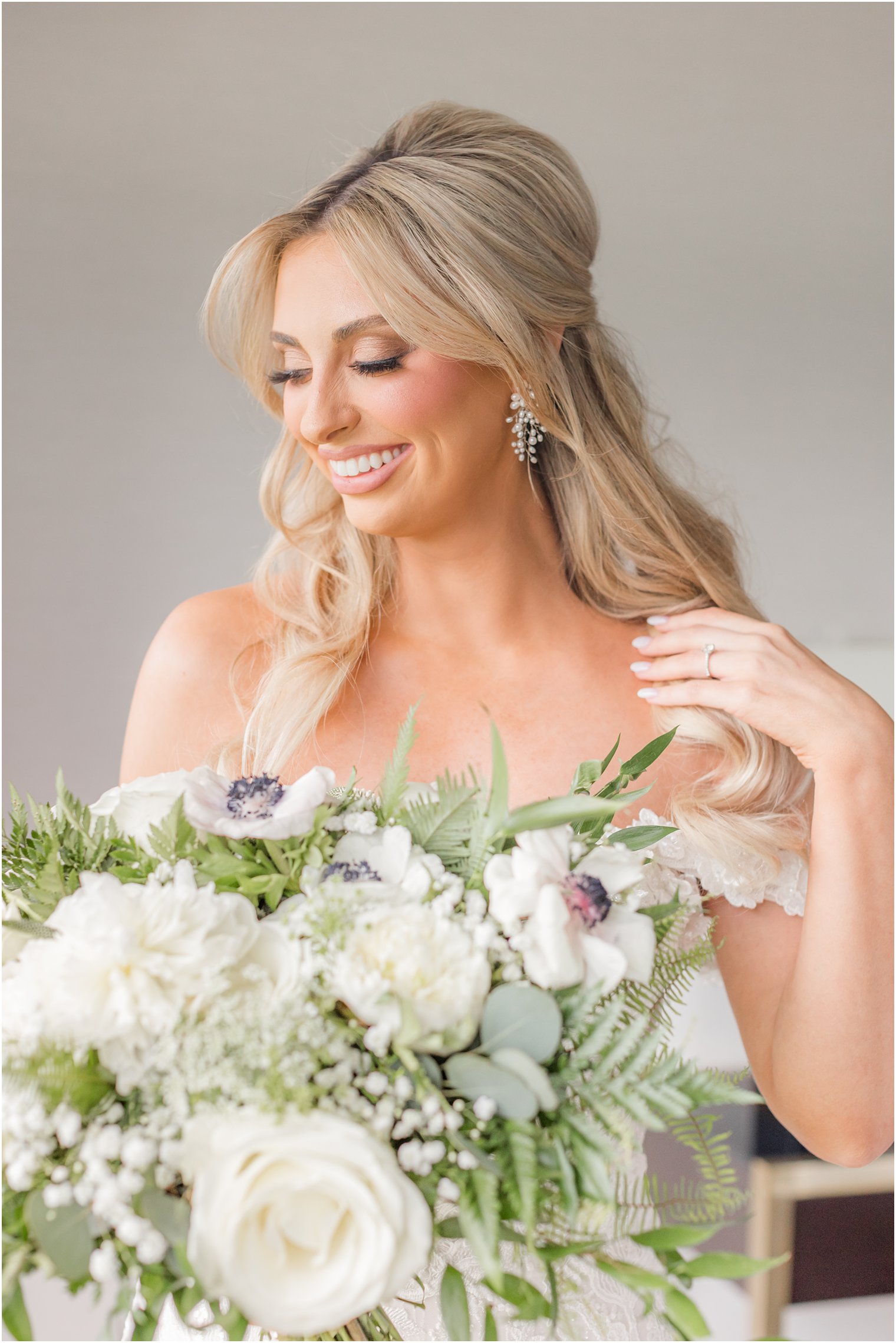 bride pushes blonde hair over shoulder holding bouquet in front of her