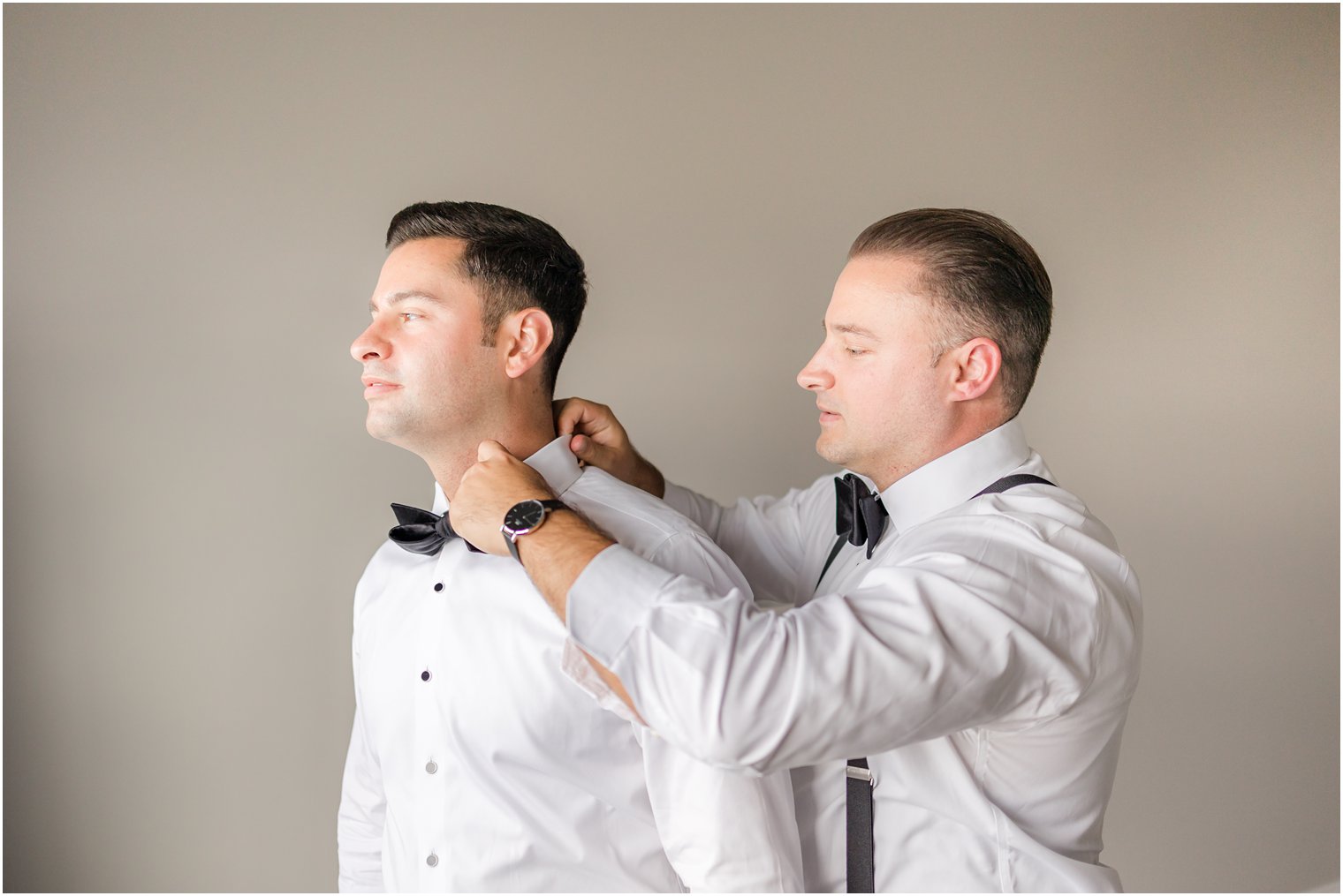 groomsman helps groom with black bowtie before garden style wedding at The English Manor