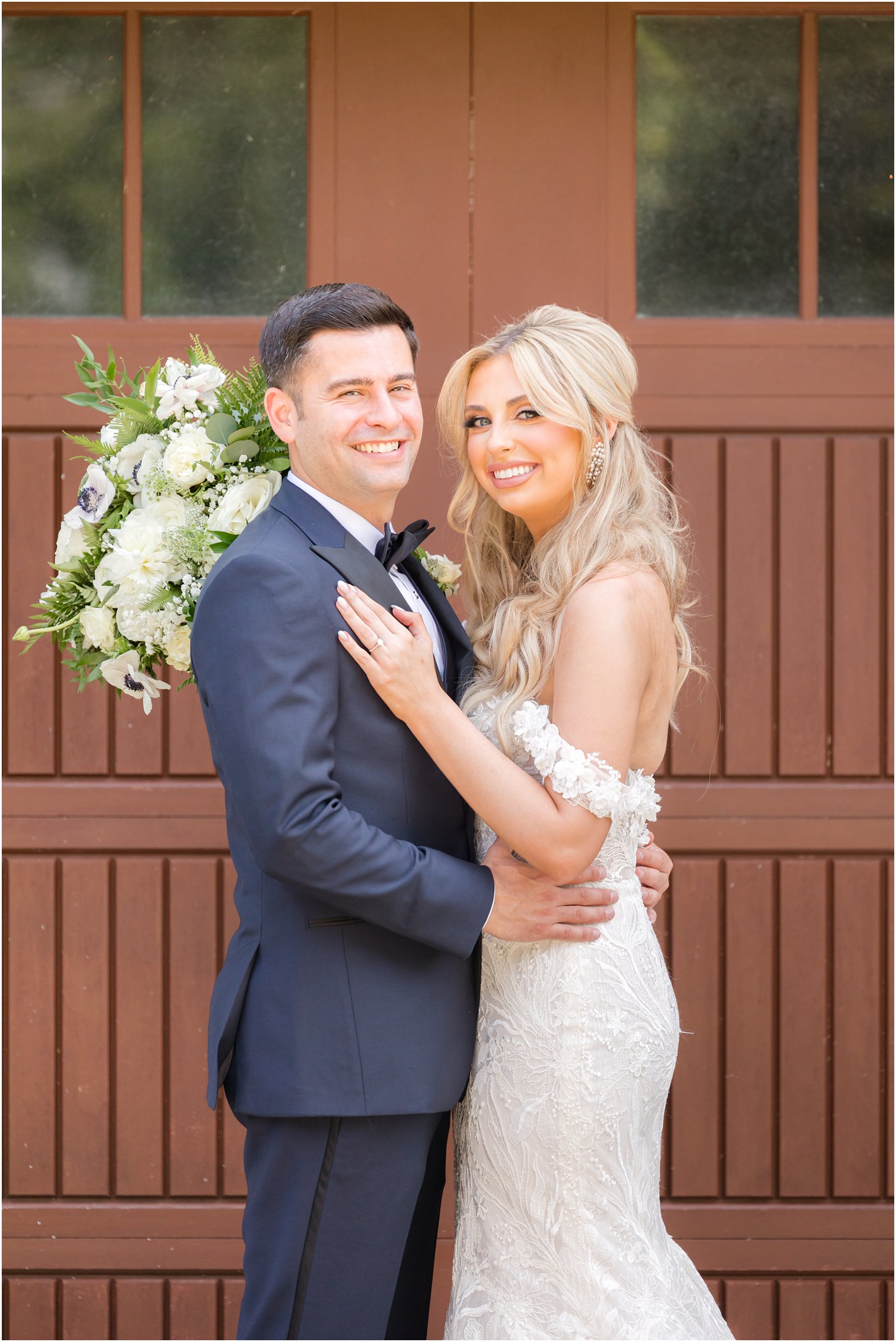 bride hugs groom with ivory bouquet behind him in front of wooden doors at The English Manor