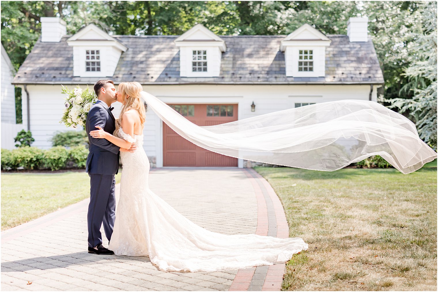 bride and groom kiss outside manor house at The English Manor with veil floating behind bride 