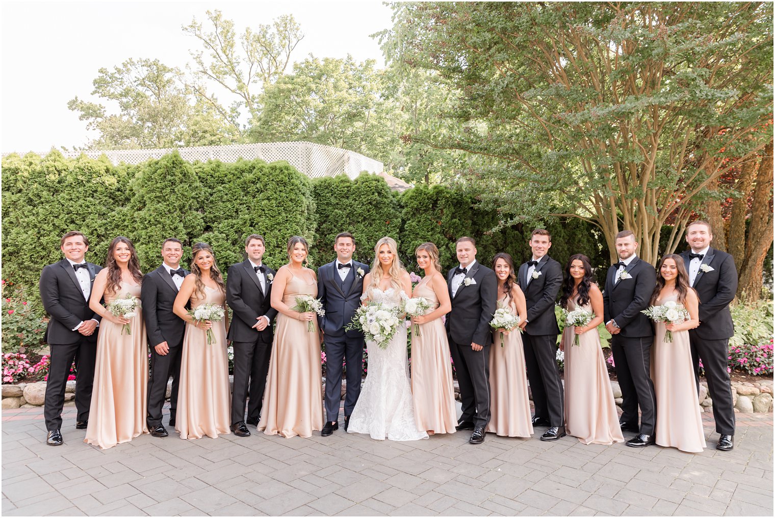 bride and groom pose with wedding party in black suits and champagne gowns 