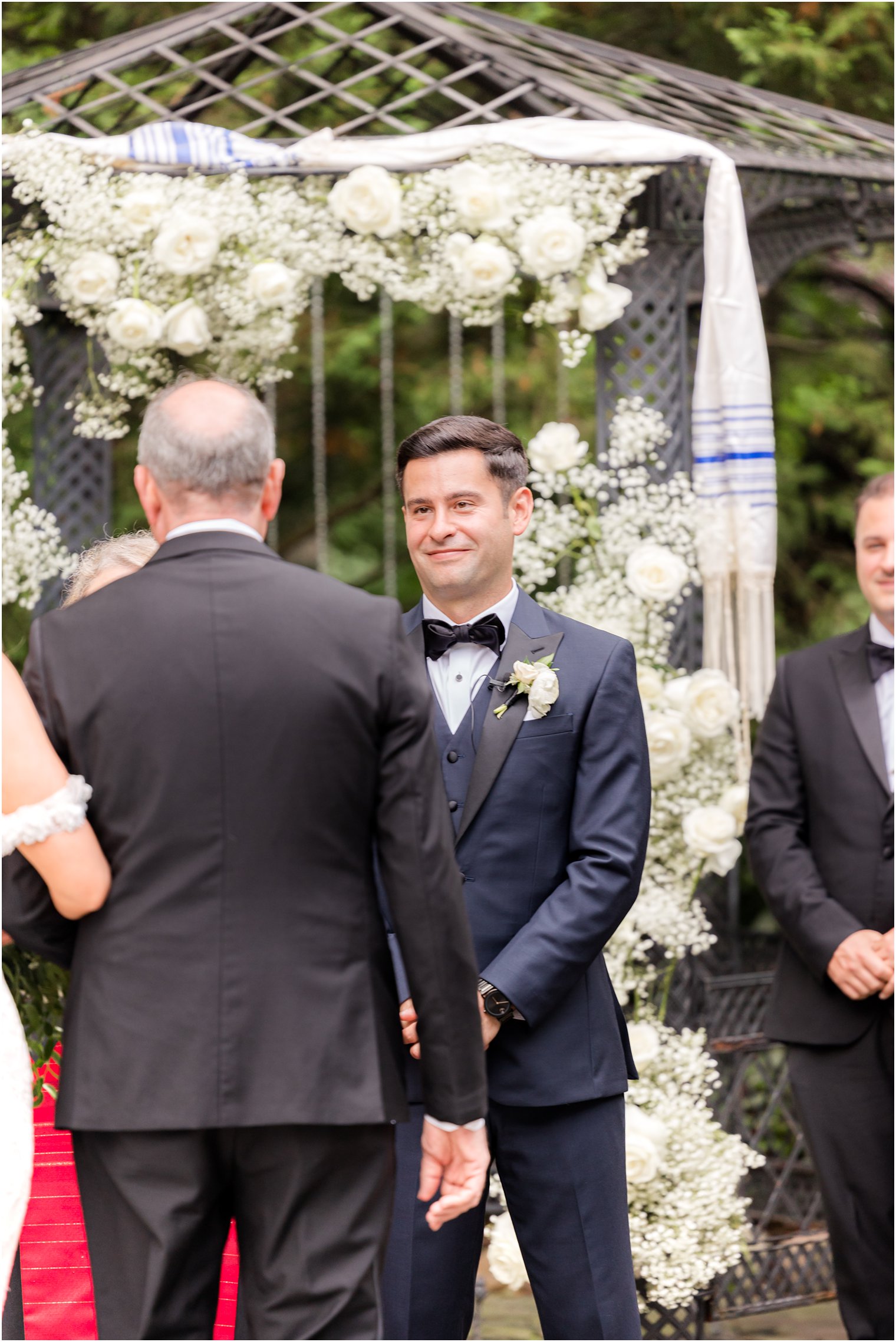 groom in blue suit with black lapels watches bride walk down aisle at The English Manor