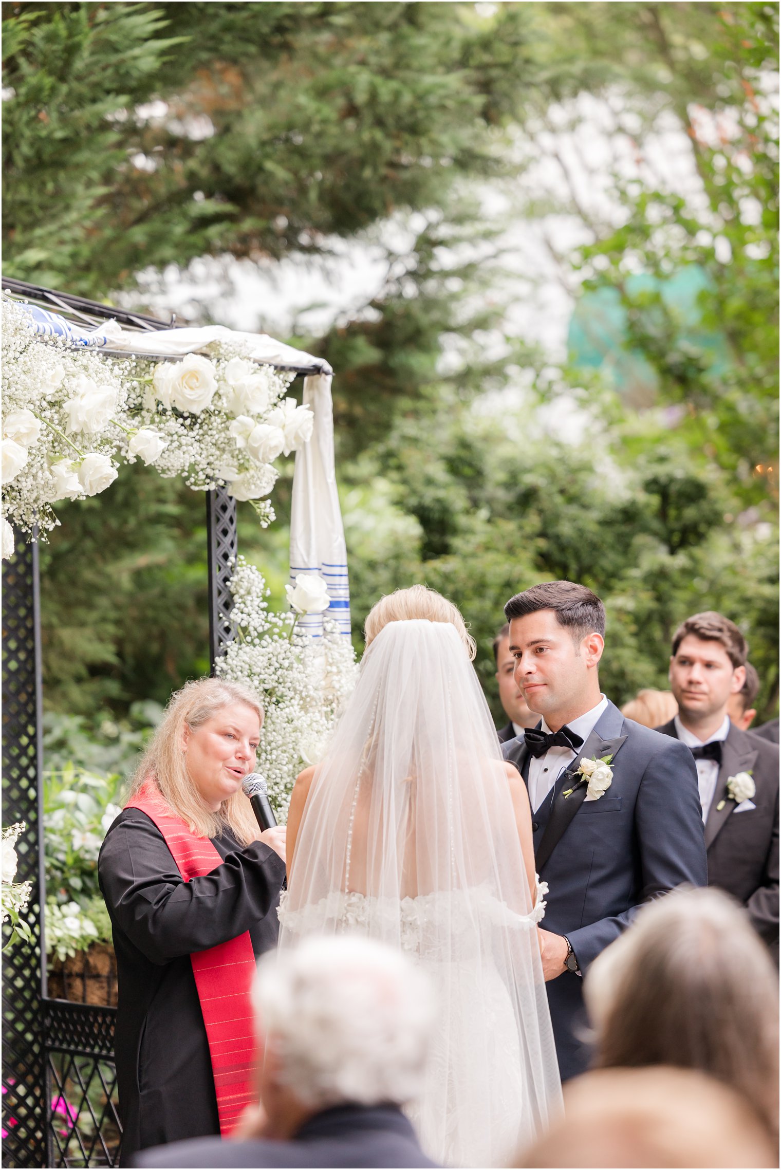 officiant speaks to bride and groom during Jewish wedding ceremony in garden 