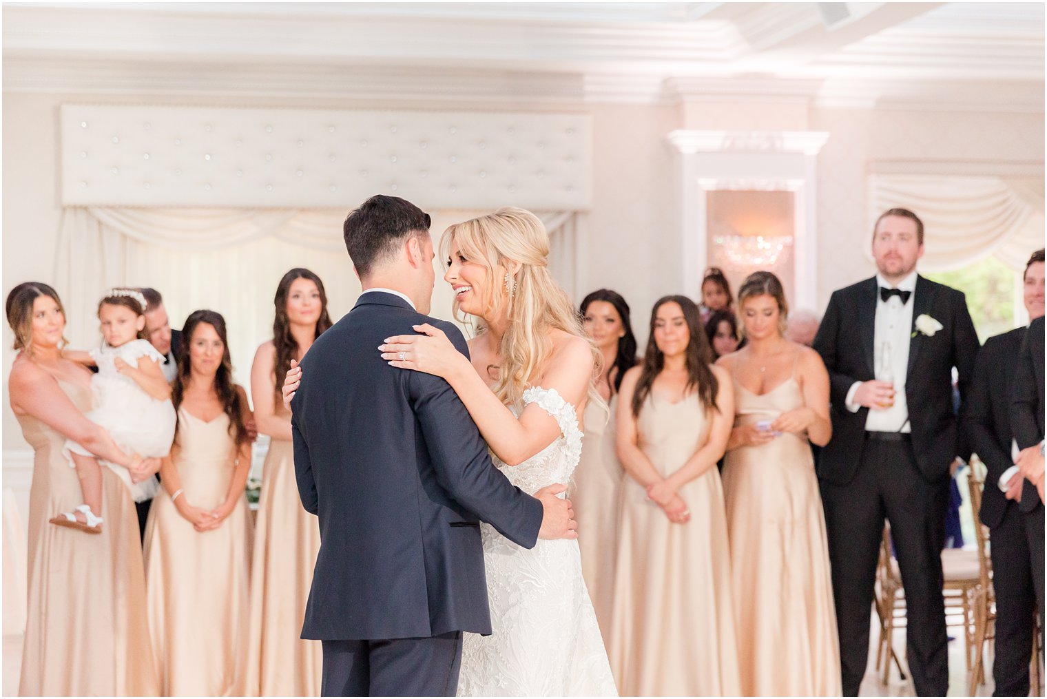 bride and groom have first dance in ballroom surrounded by wedding party