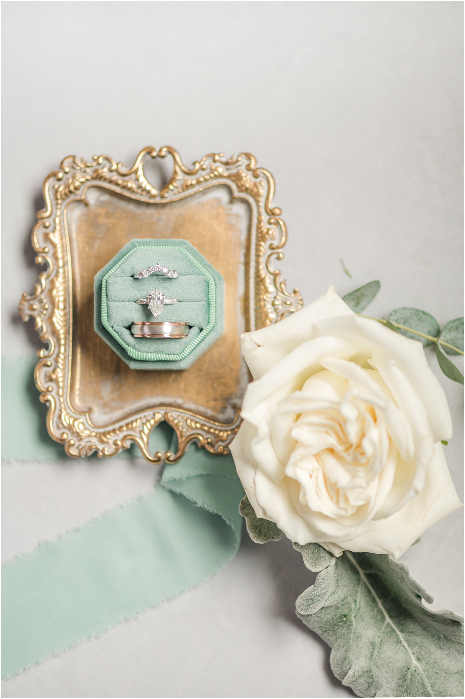 diamond rings and silver band rest in mint green ring box on gold tray 