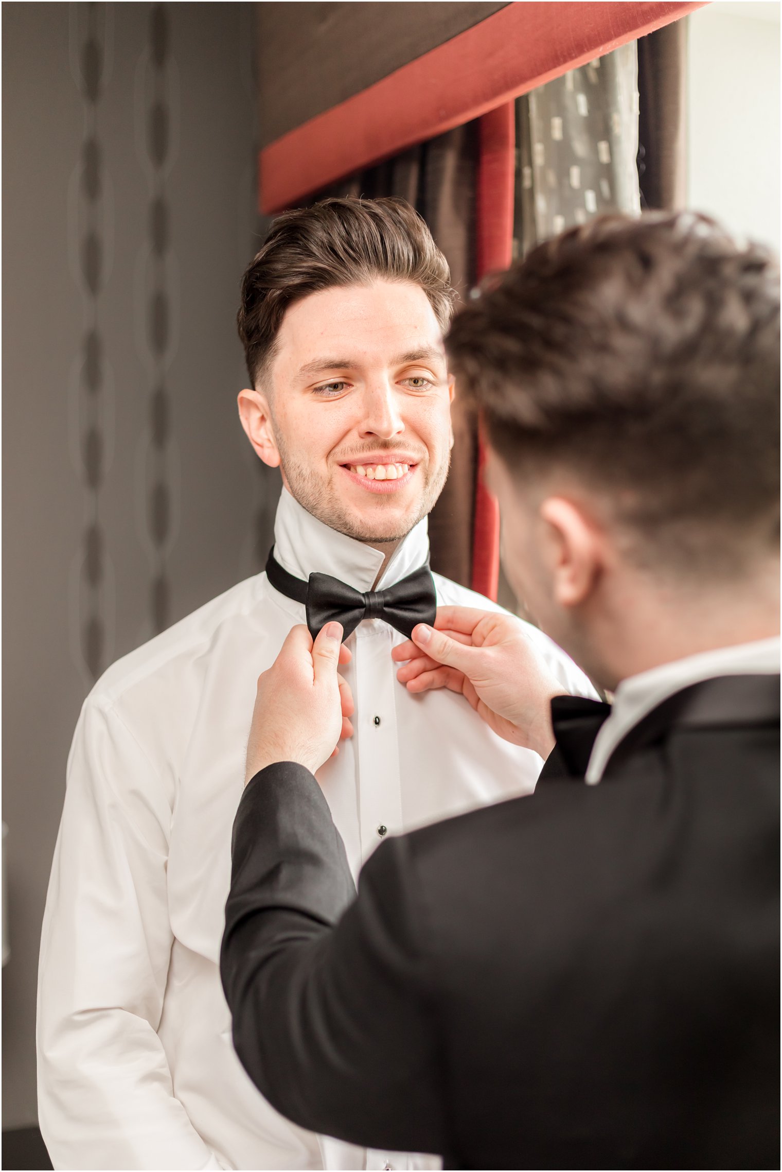 groomsman helps groom with bowtie for wedding day 