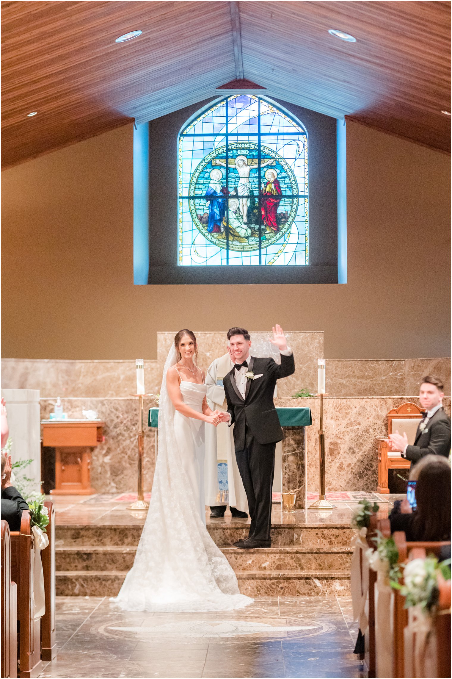 bride and groom smile at guests standing at alter during traditional church ceremony in small New Jersey church