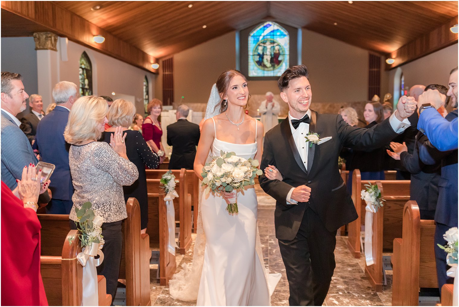 bride and groom smile and fist bump guests leaving  traditional church ceremony in small New Jersey church