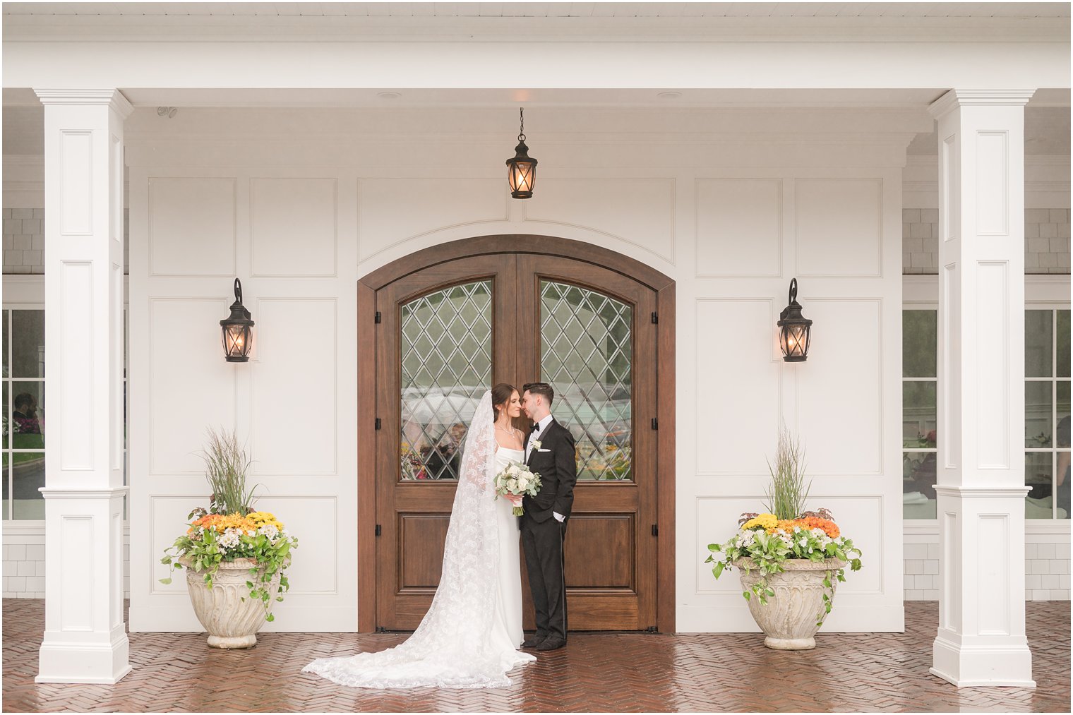 newlyweds stand by wooden doors hugging with bride's detailed veil around her back 