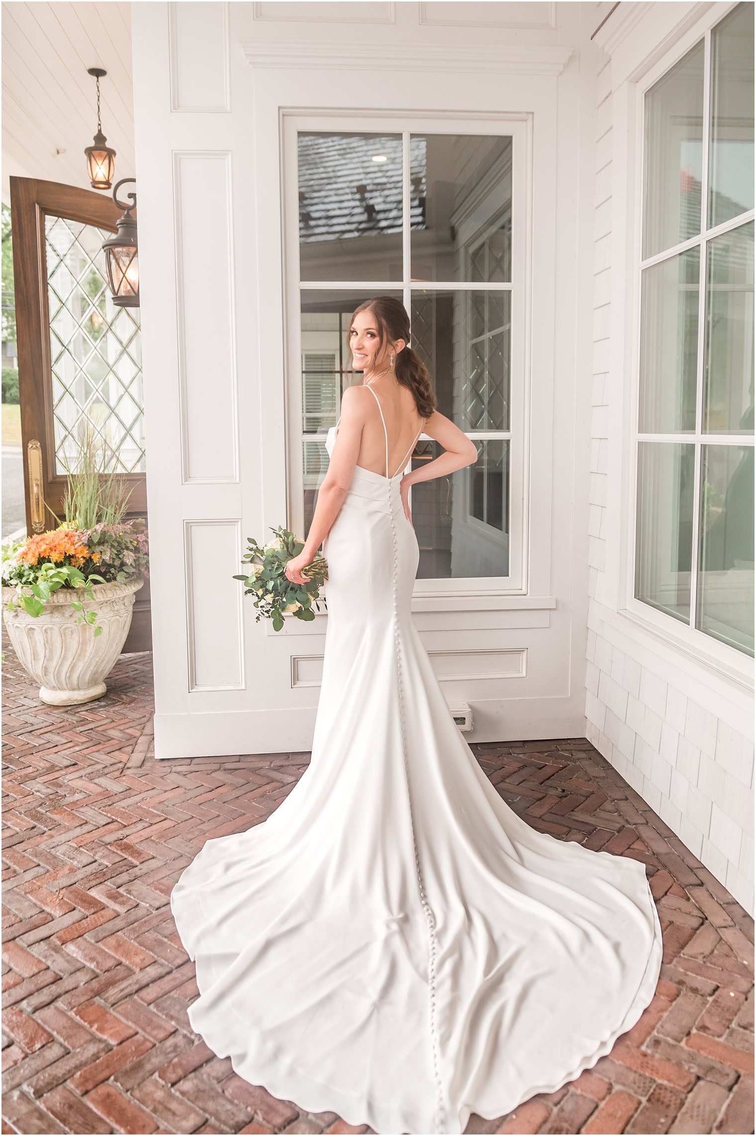 bride poses by big windows at The Mill Lakeside Manor showing off back of wedding gown 