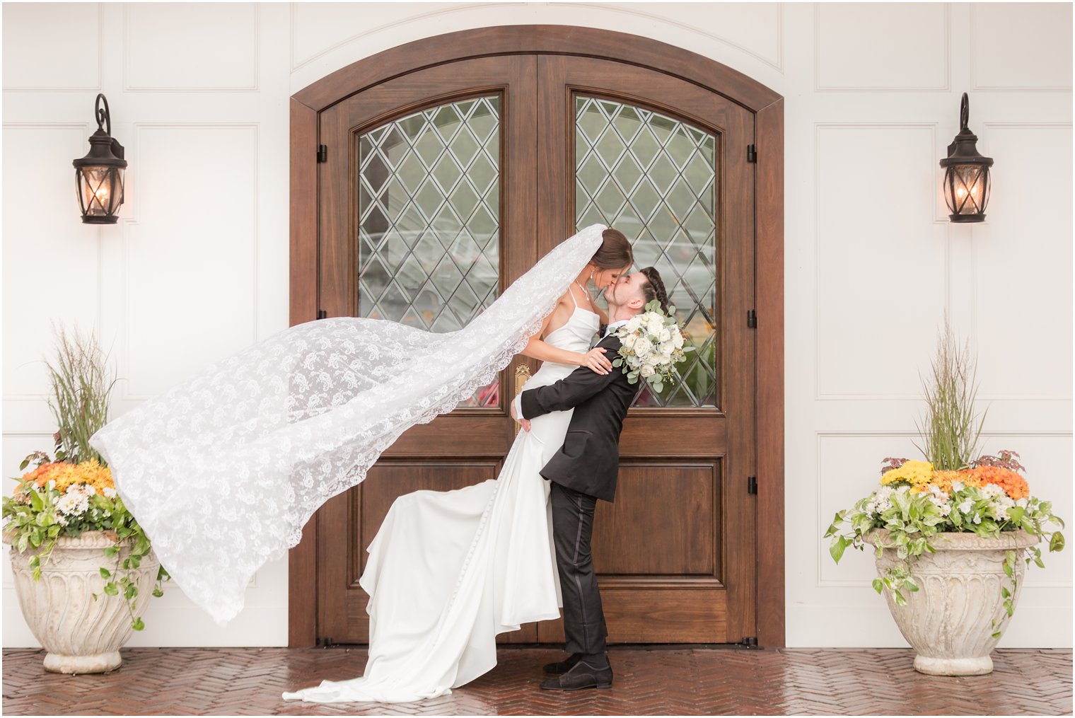 groom lifts bride up with veil floating behind her kissing her by wooden door at The Mill Lakeside Manor