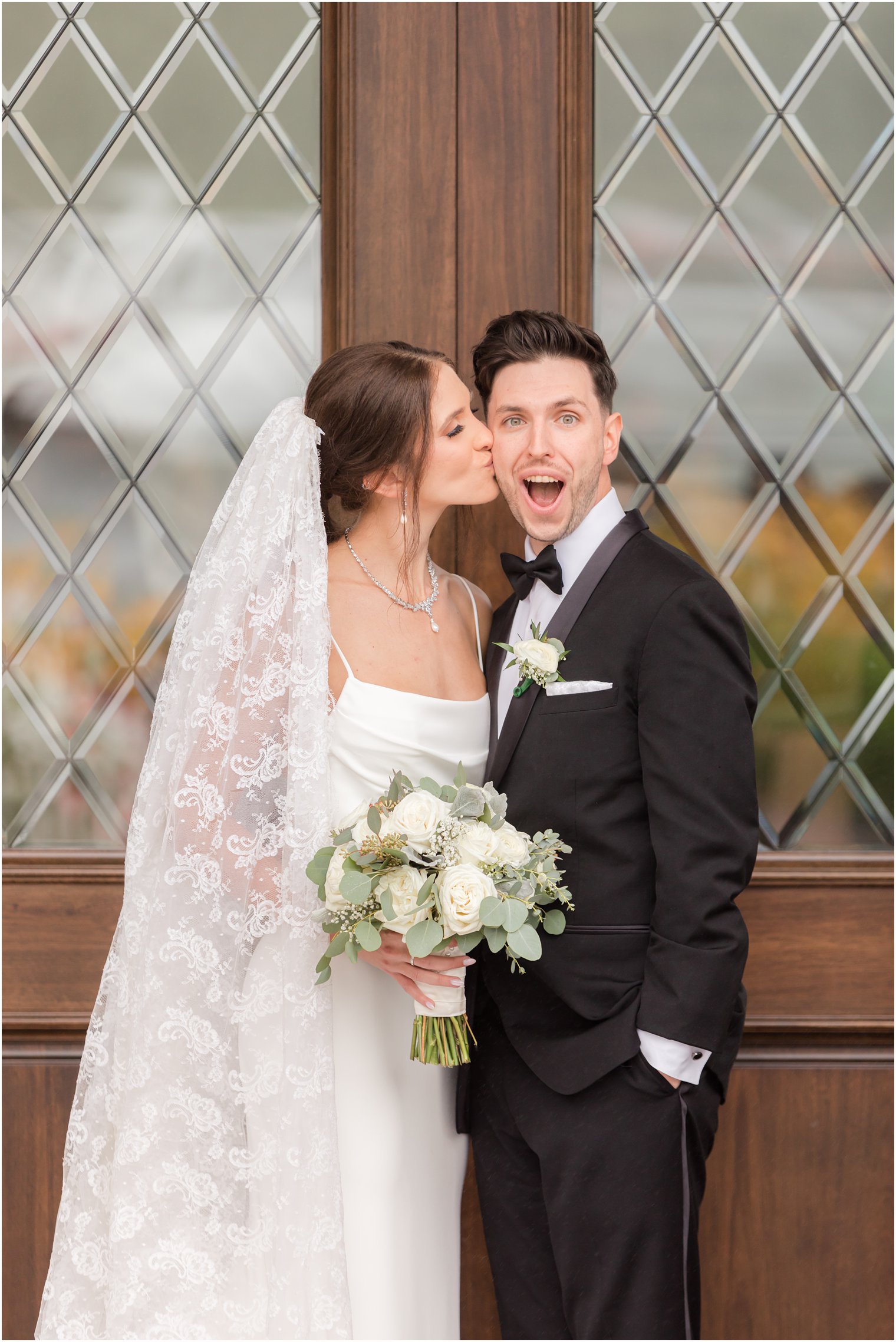 bride kisses groom's cheek by wooden doors at The Mill Lakeside Manor