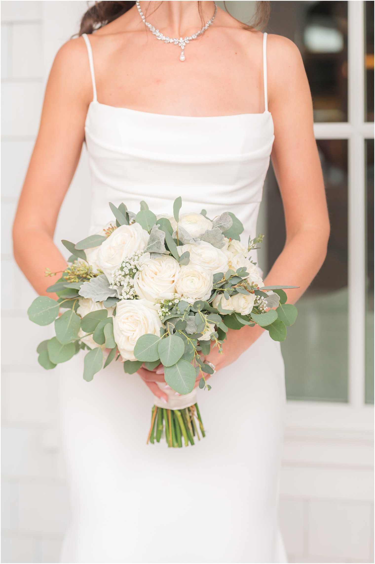 bride in sleek wedding gown holds bouquet ivory roses during rainy wedding at The Mill Lakeside Manor