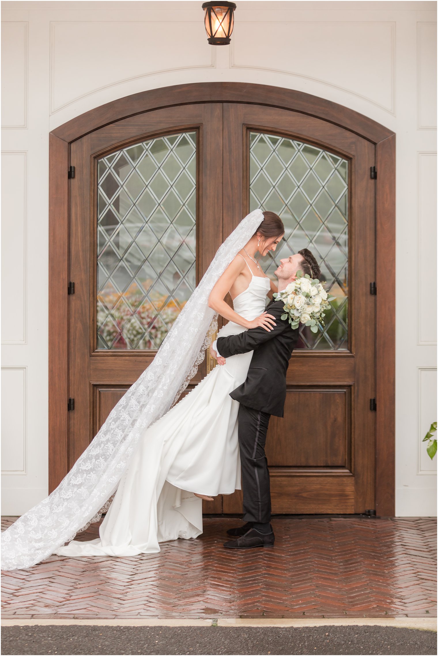 groom lifts up bride by wooden door with veil trailing behind her at The Mill Lakeside Manor