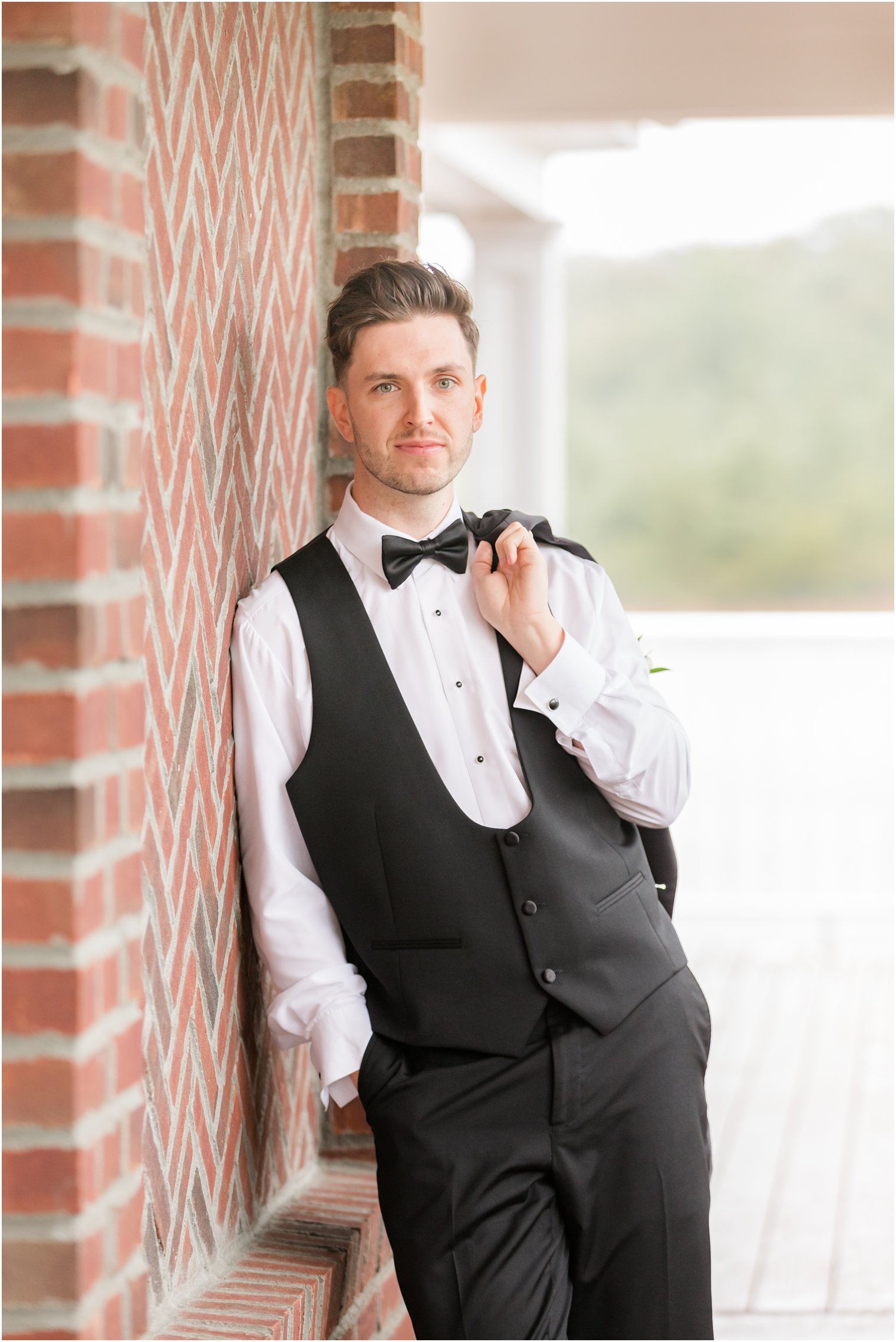 groom leans against brick wall with black jacket over shoulder at The Mill Lakeside Manor