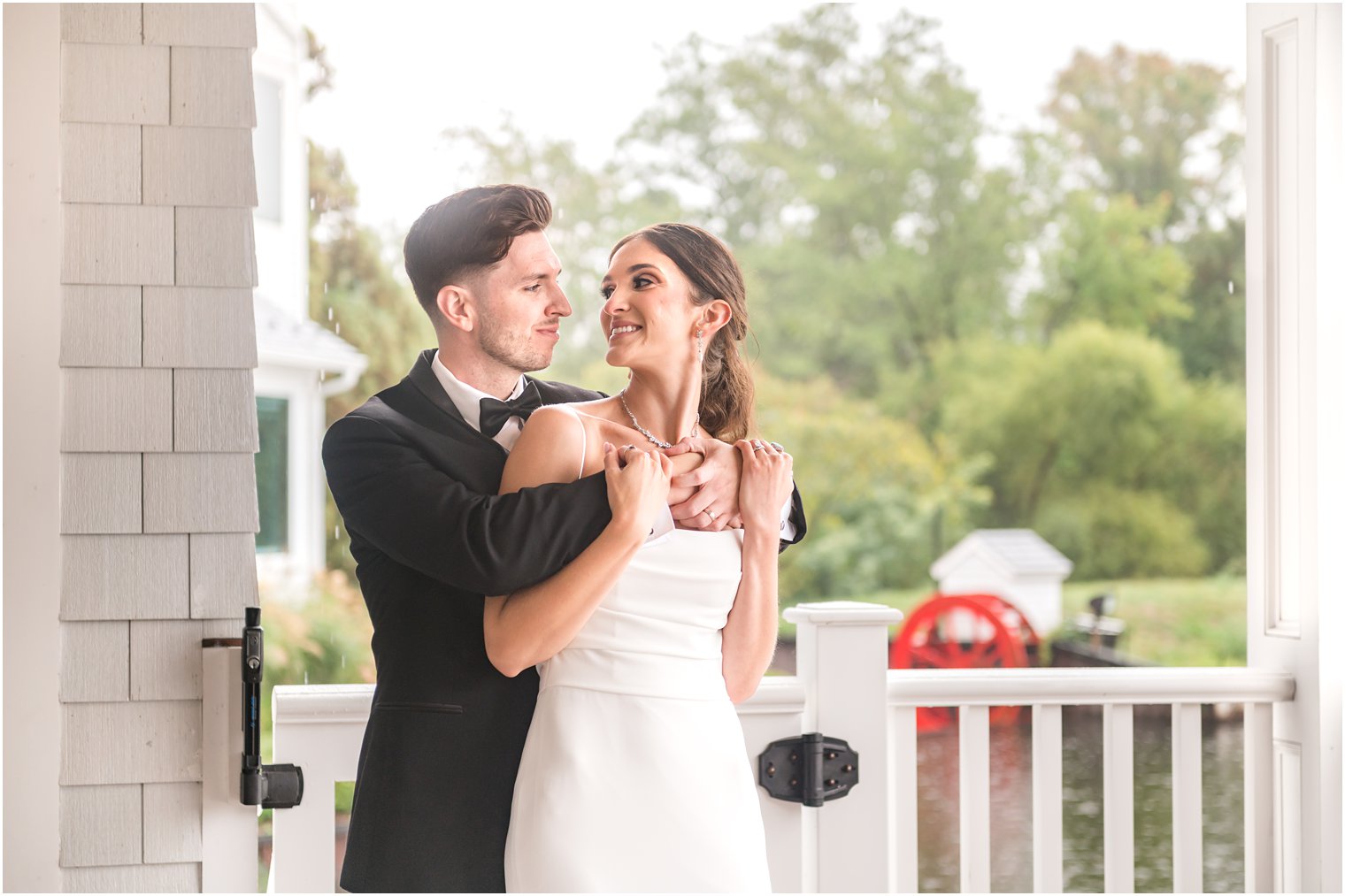groom hugs bride around shoulders standing on patio by lake at The Mill Lakeside Manor