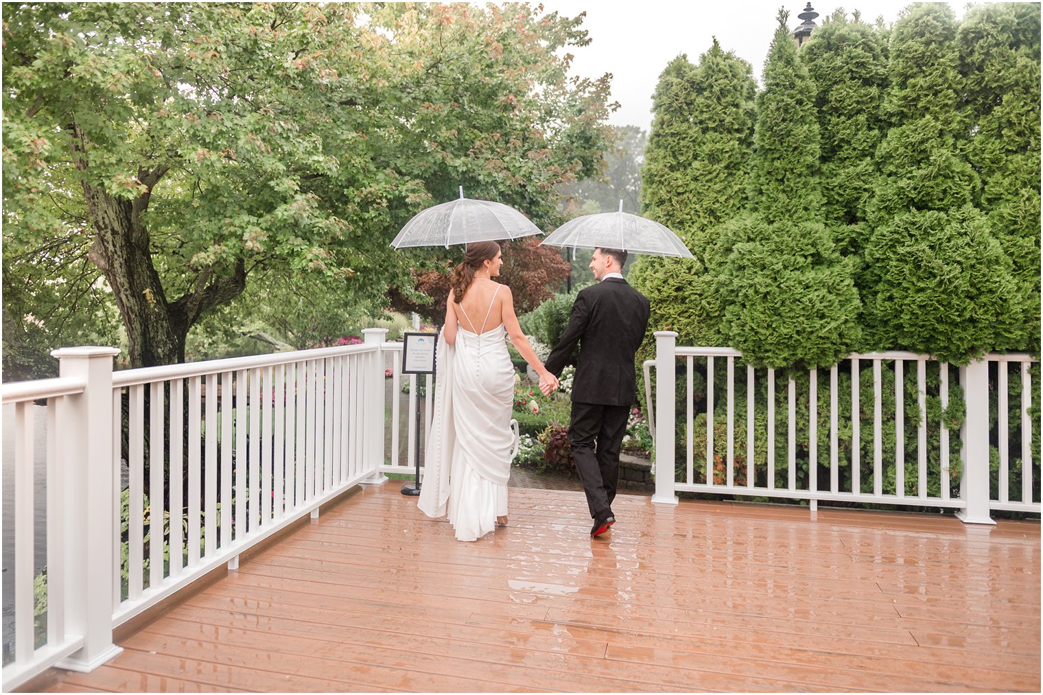 newlyweds hold hands under clear umbrellas on patio at The Mill Lakeside Manor