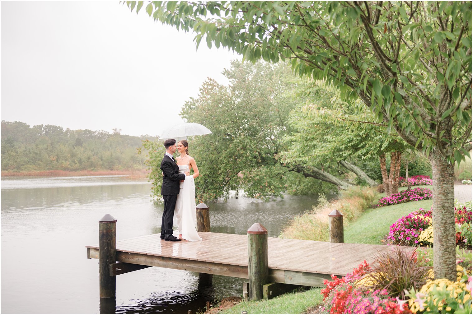 bride and groom hug under clear umbrella on wooden dock at The Mill Lakeside Manor