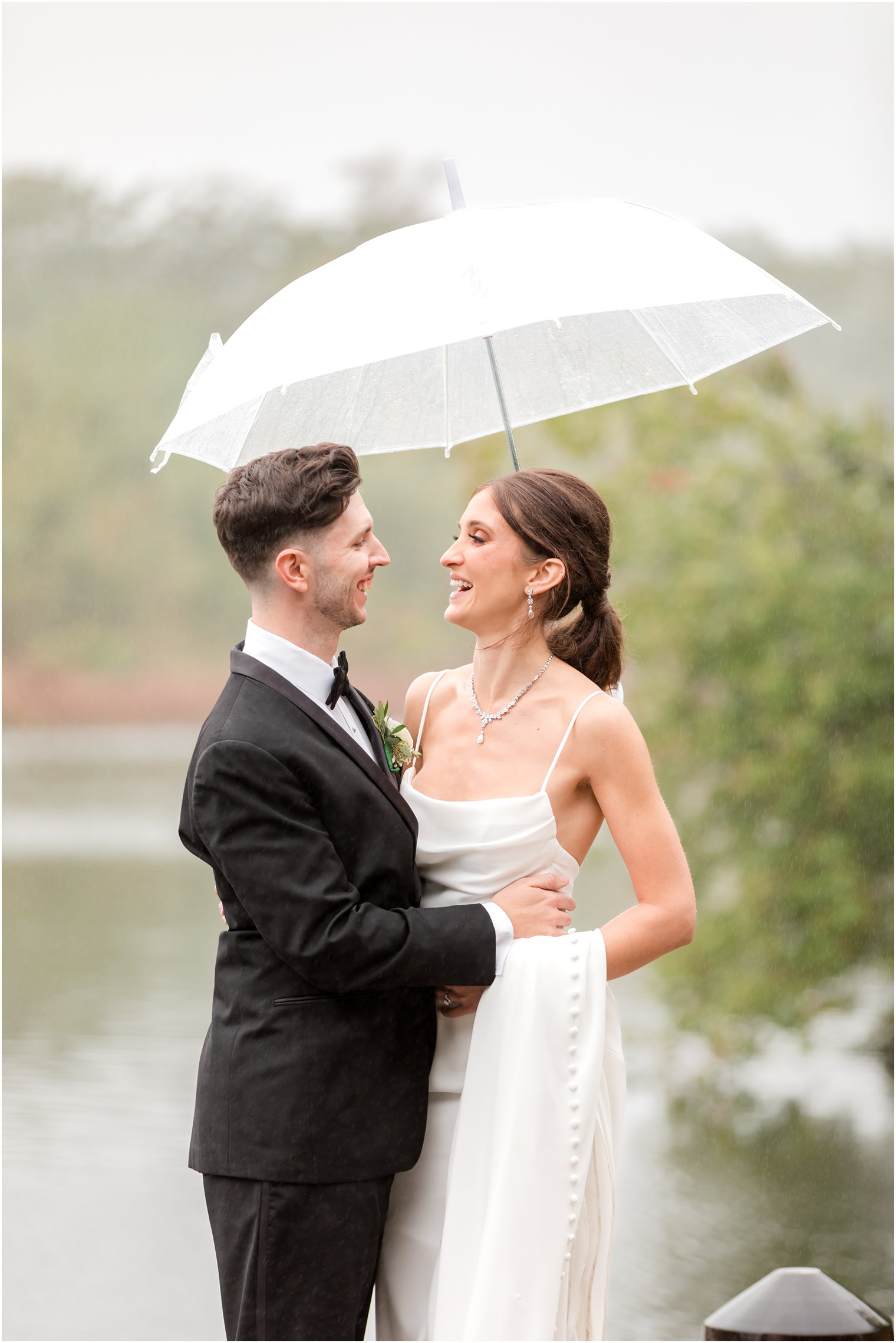 newlyweds laugh under umbrella on rainy wedding day at The Mill Lakeside Manor