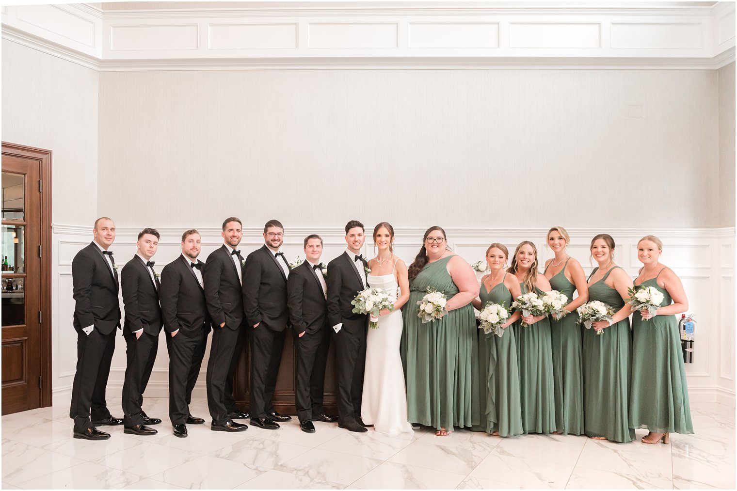 newlyweds stand with wedding party in black tuxes and sage green gowns at The Mill Lakeside Manor