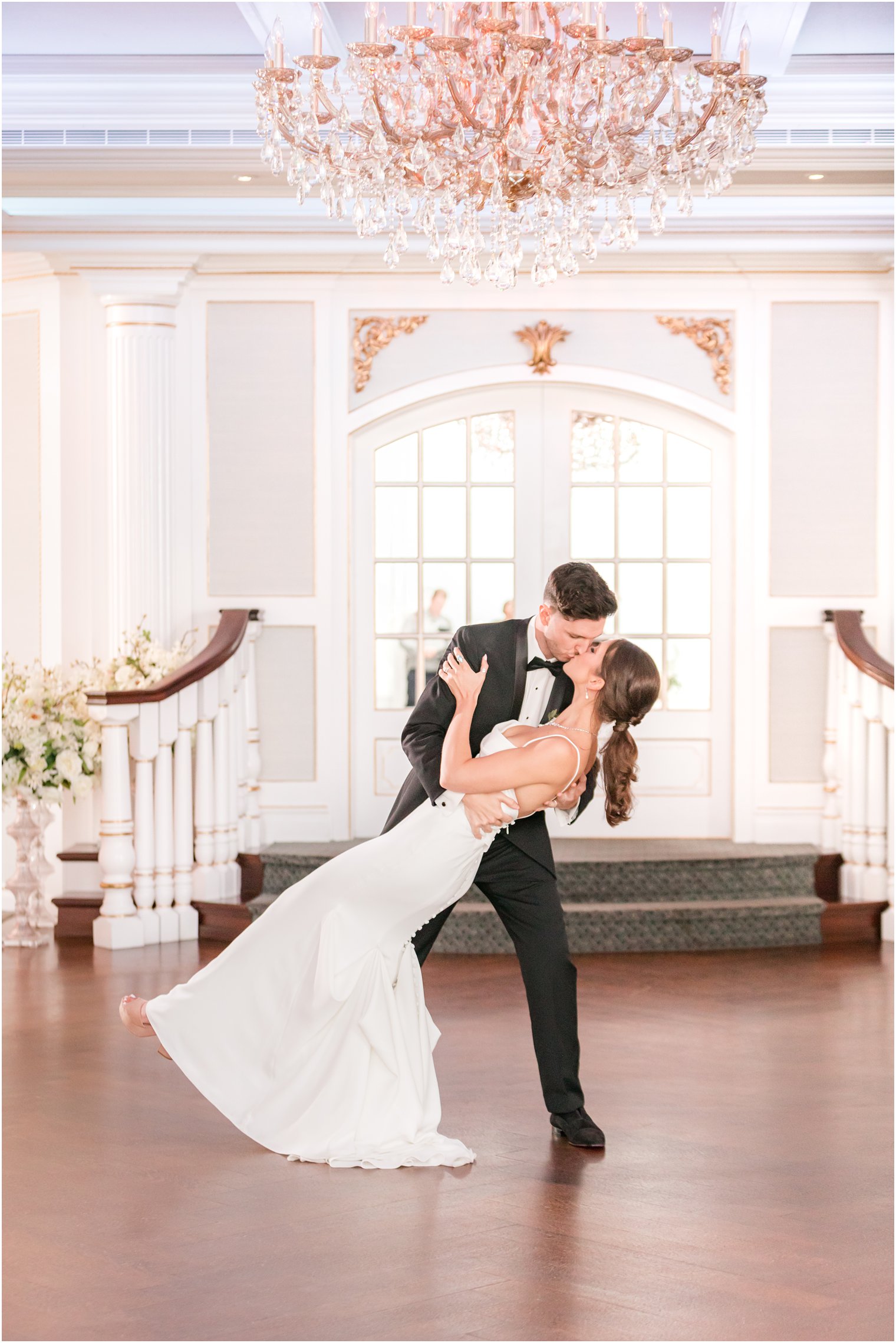 groom kisses bride dipping her under chandelier in ballroom at The Mill Lakeside Manor