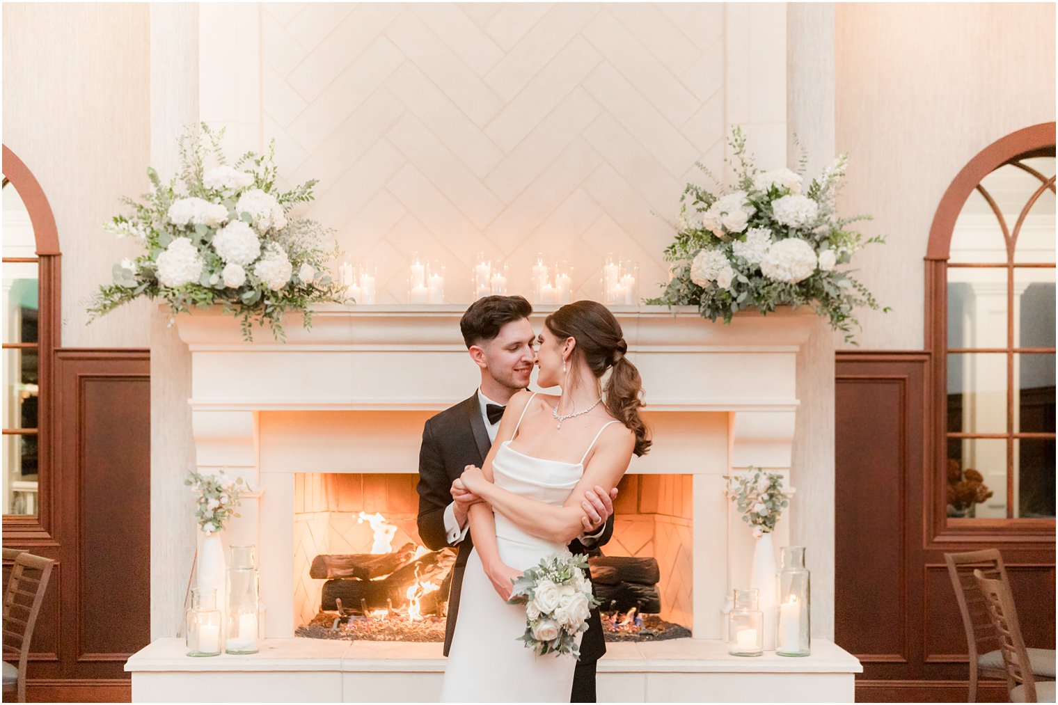 bride and groom nuzzle noses in front of white fireplace lined with candles at The Mill Lakeside Manor