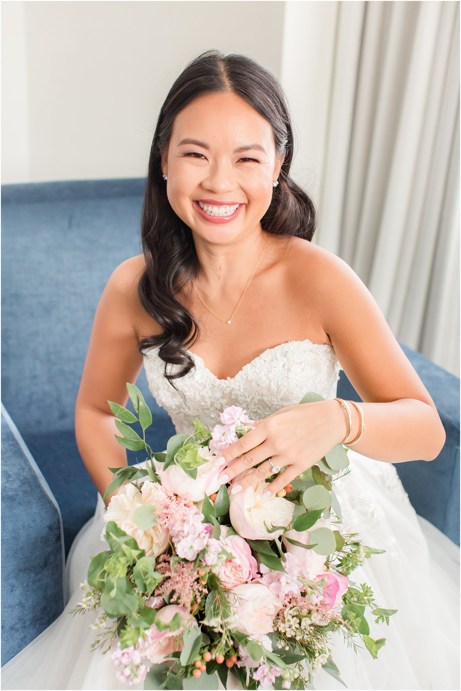 bride sits in blue chair holding bouquet of pink and white flowers in Philly PA