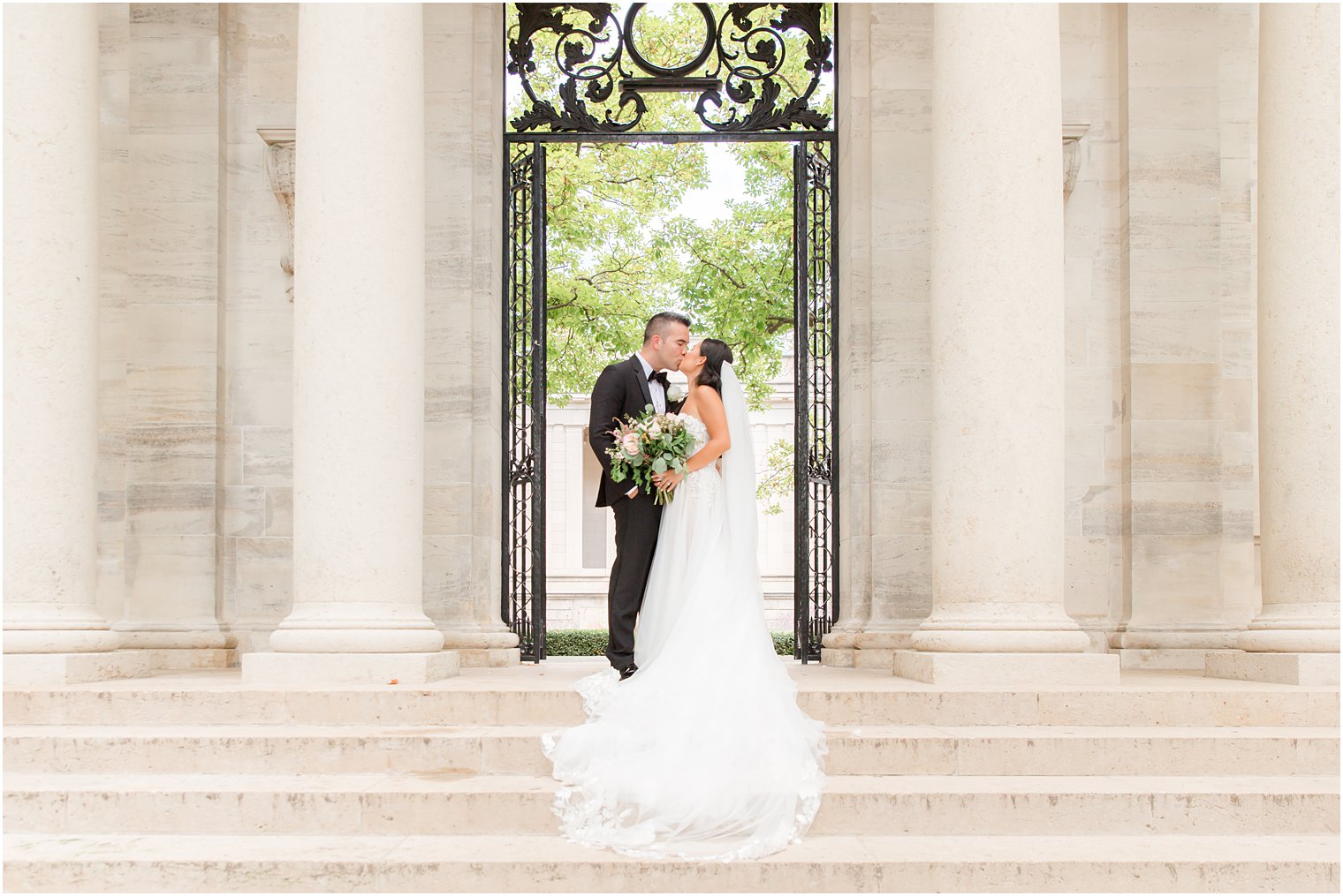 bride and groom kiss on steps between columns at the Rodin Museum