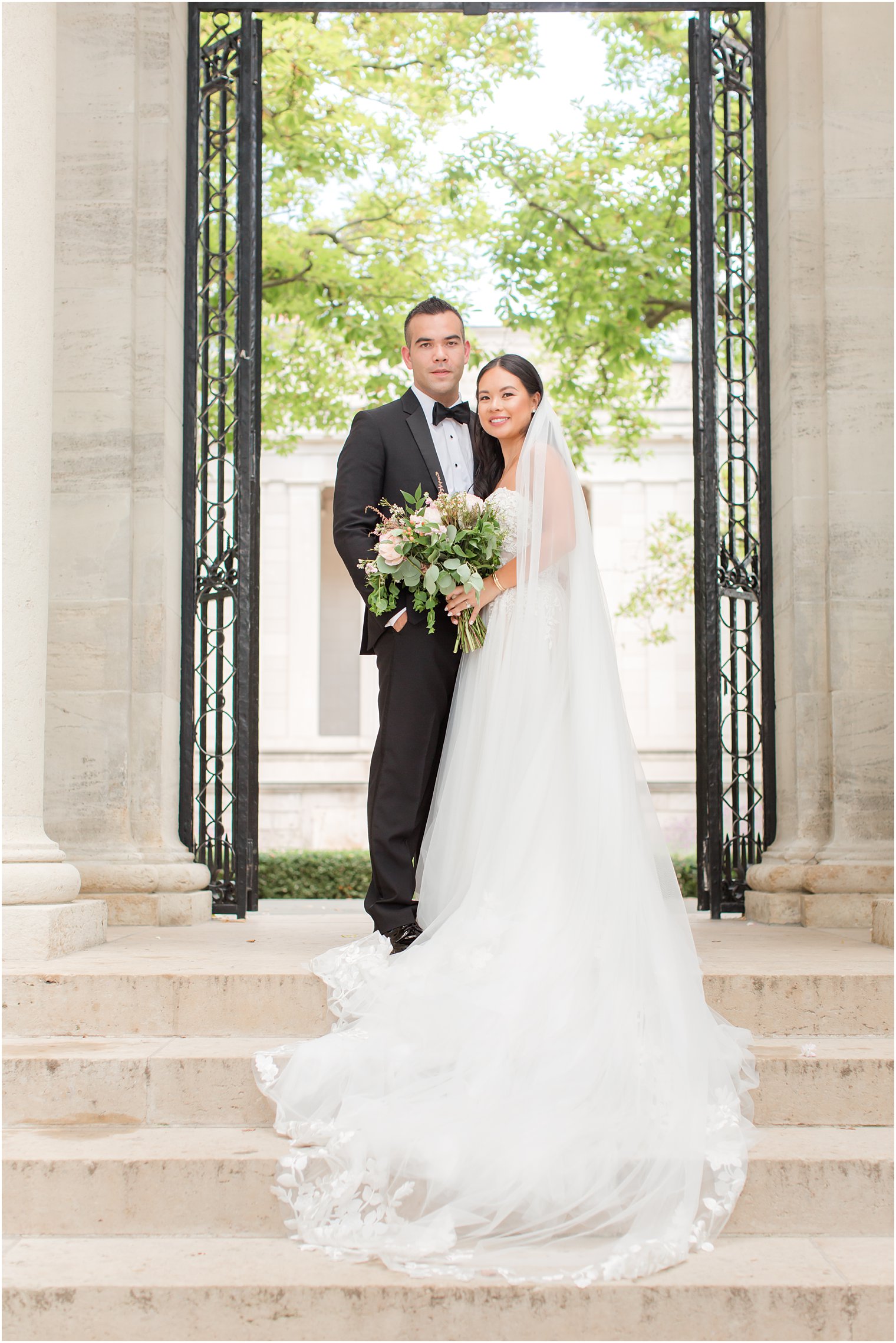 newlyweds stand on steps between iron gates at the Rodin Museum
