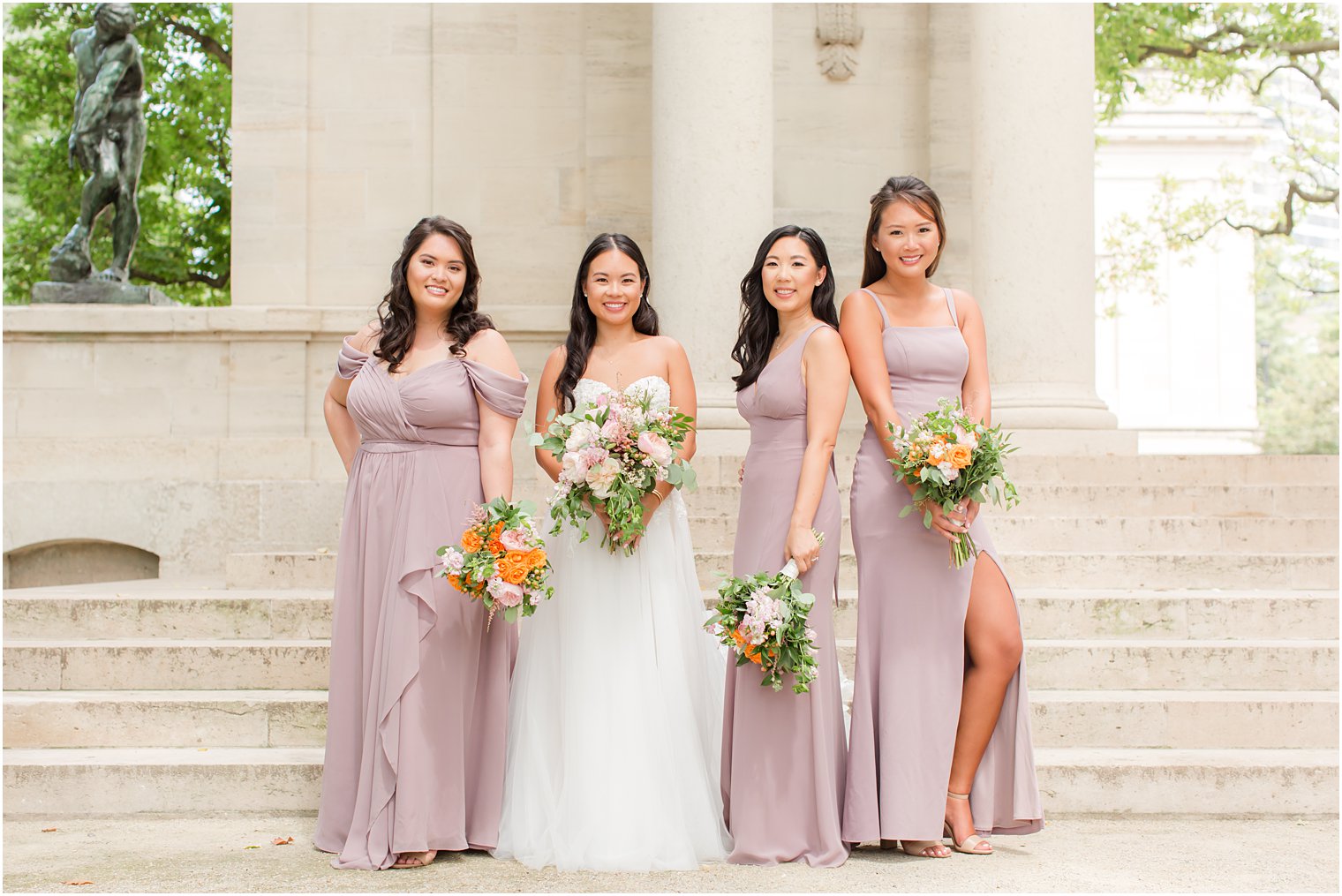 bride stands with bridesmaids in mauve gowns on steps at the Rodin Museum