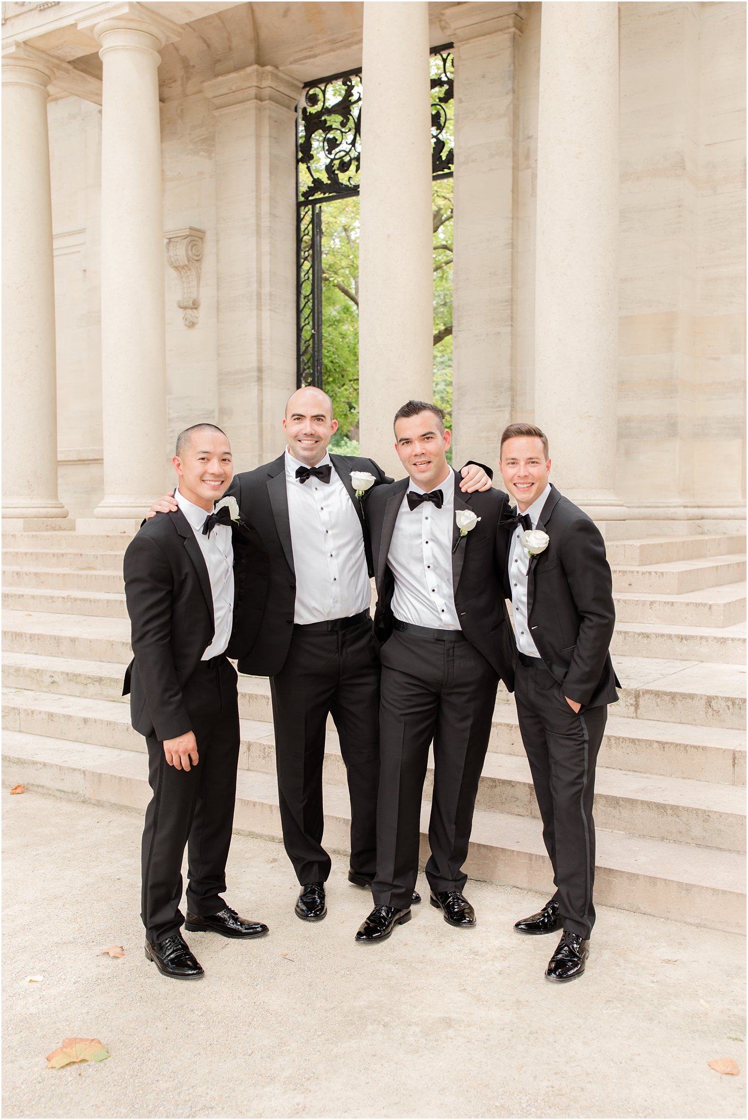 groom hugs groomsmen in black tuxes on steps at the Rodin Museum