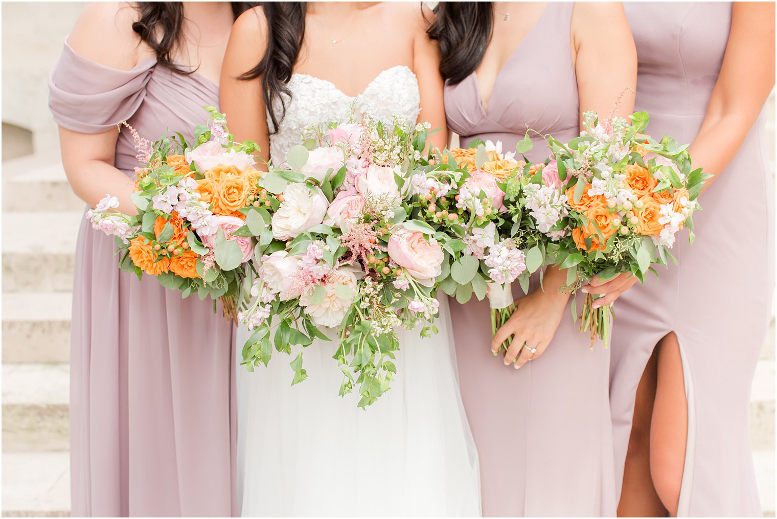 bride stands with bridesmaids in mauve gowns holding bouquets with orange flowers 