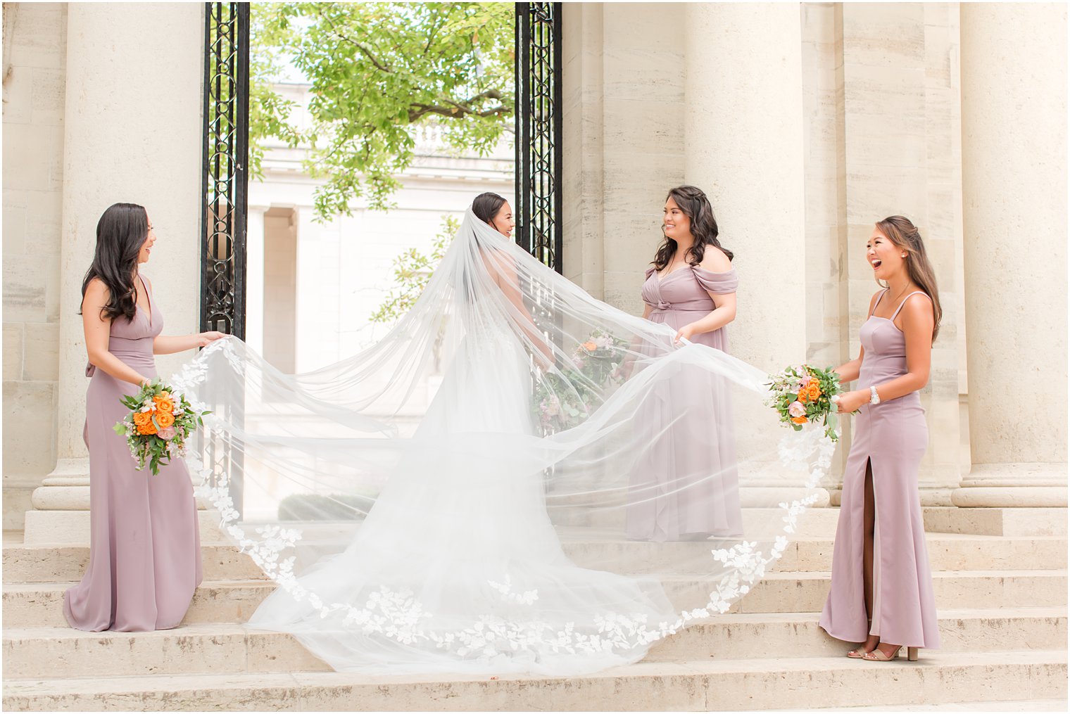 bridesmaids help pull bride's veil around her on steps at the Rodin Museum